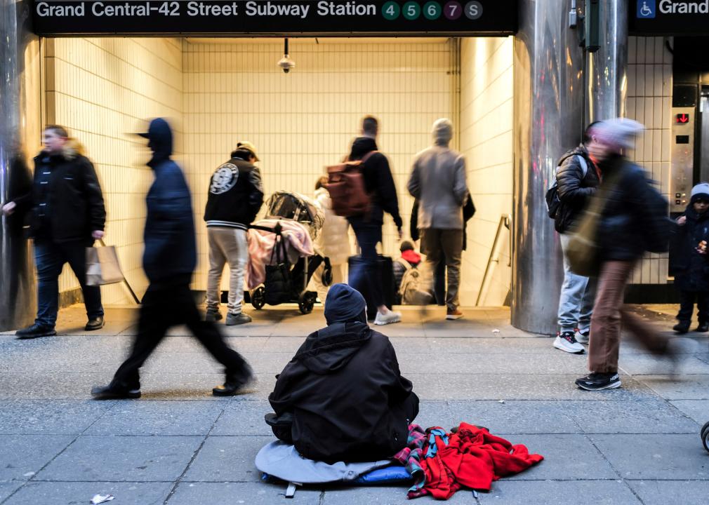 People walk past a man sitting on the sidewalk in front of the Grand Central-42 Street Subway Station in Manhattan.