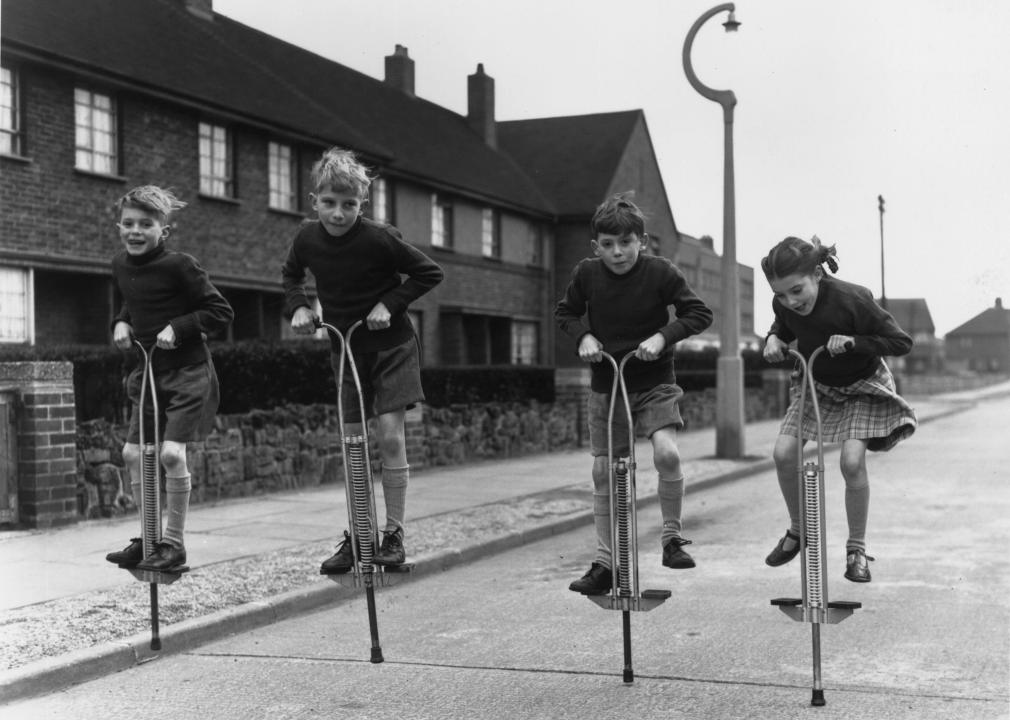 Four children play with pogo sticks in the street.