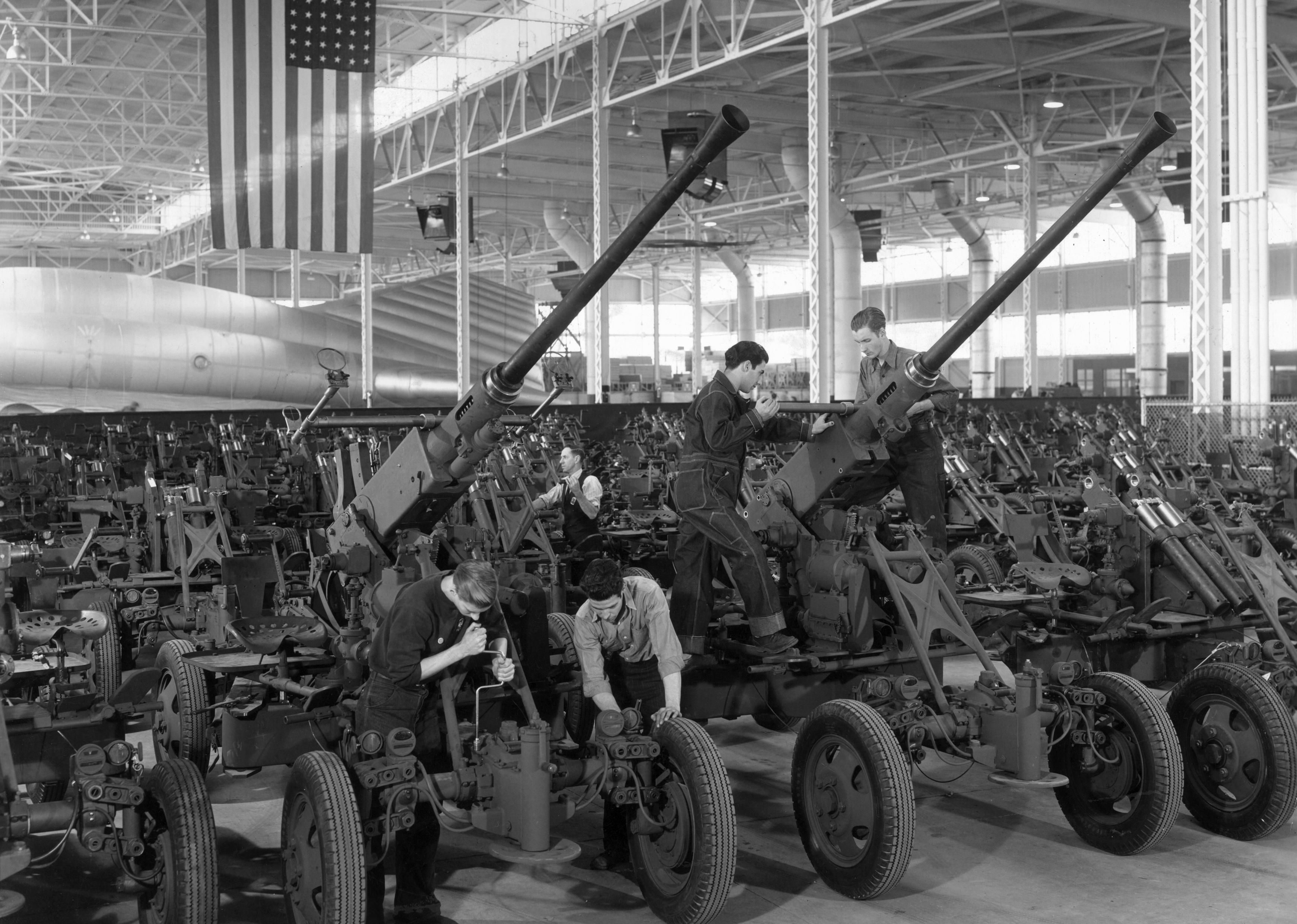 A full-length view of young male workers wearing uniforms, assembling 40 millimeter anti-aircraft guns.