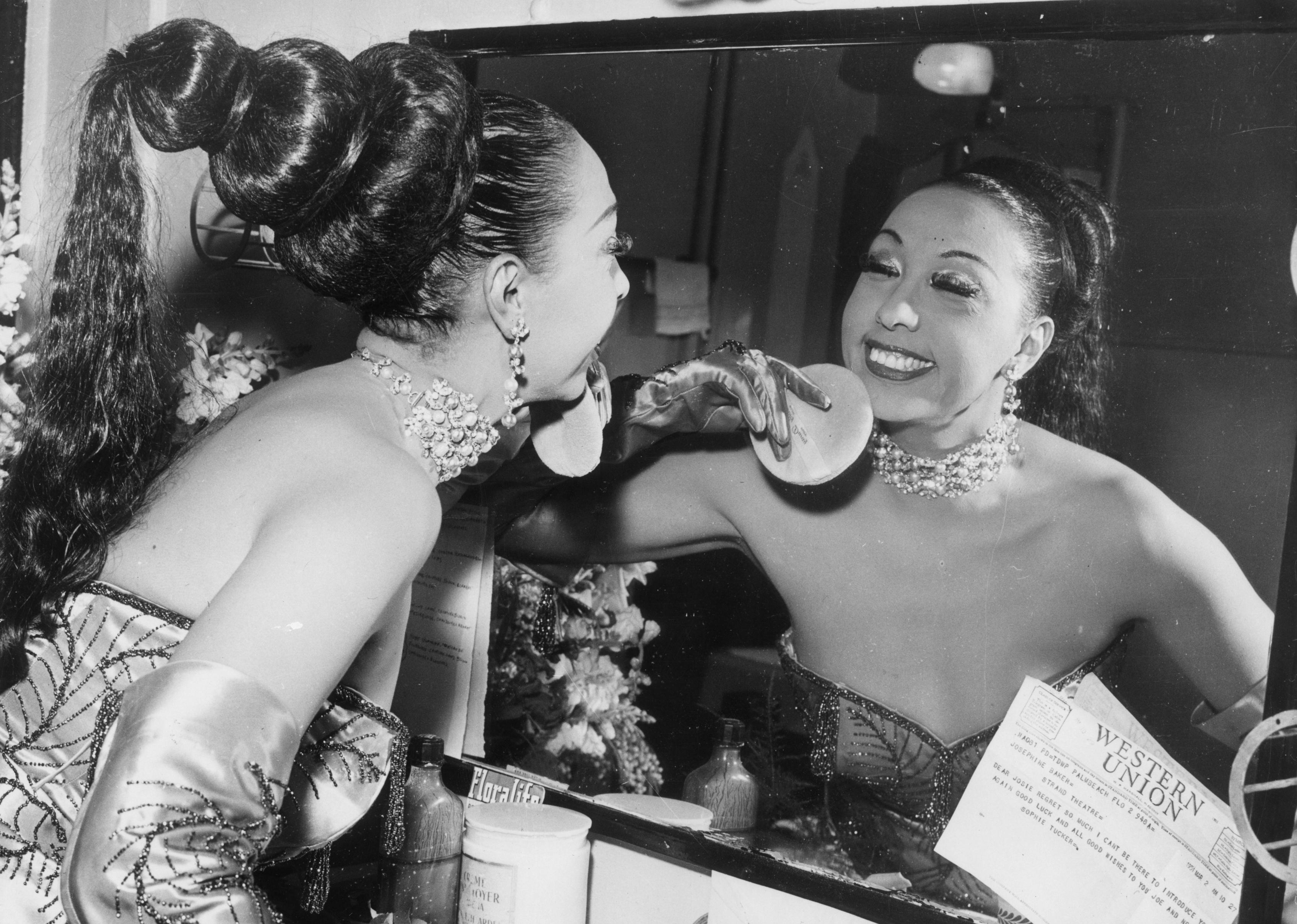 Josephine Baker applies makeup with a powder puff in her dressing room.