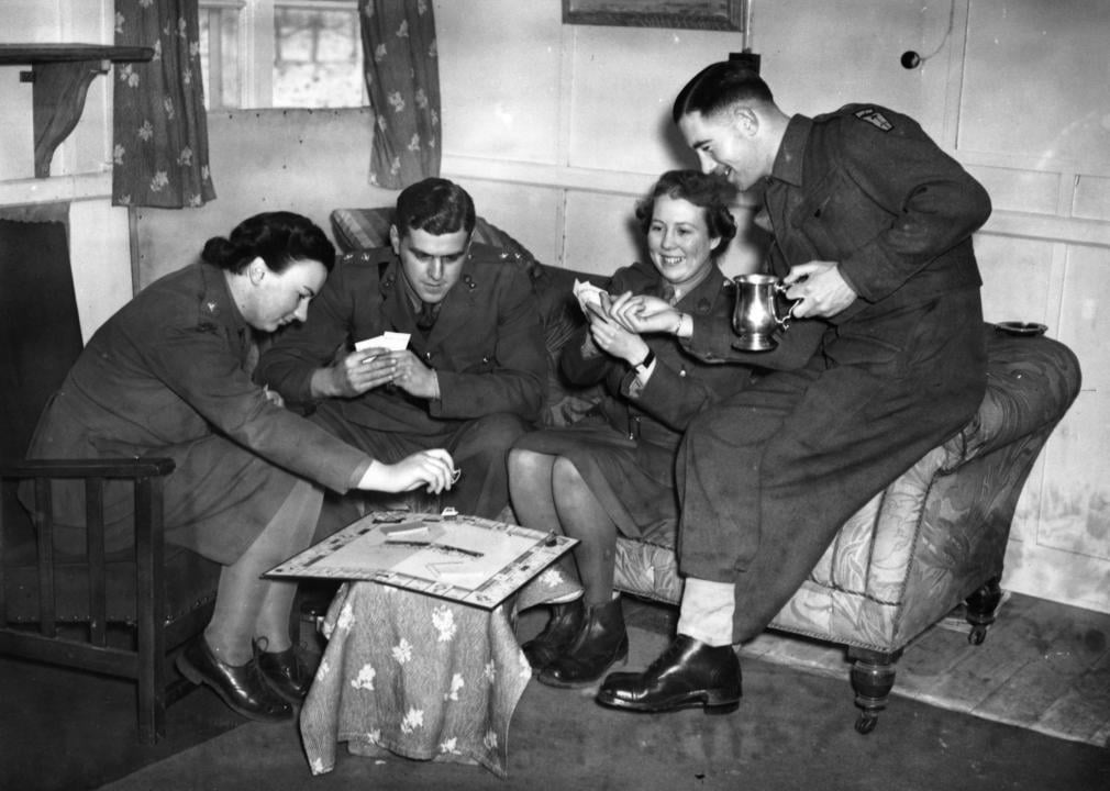 Men in military uniform play the Monopoly board game.