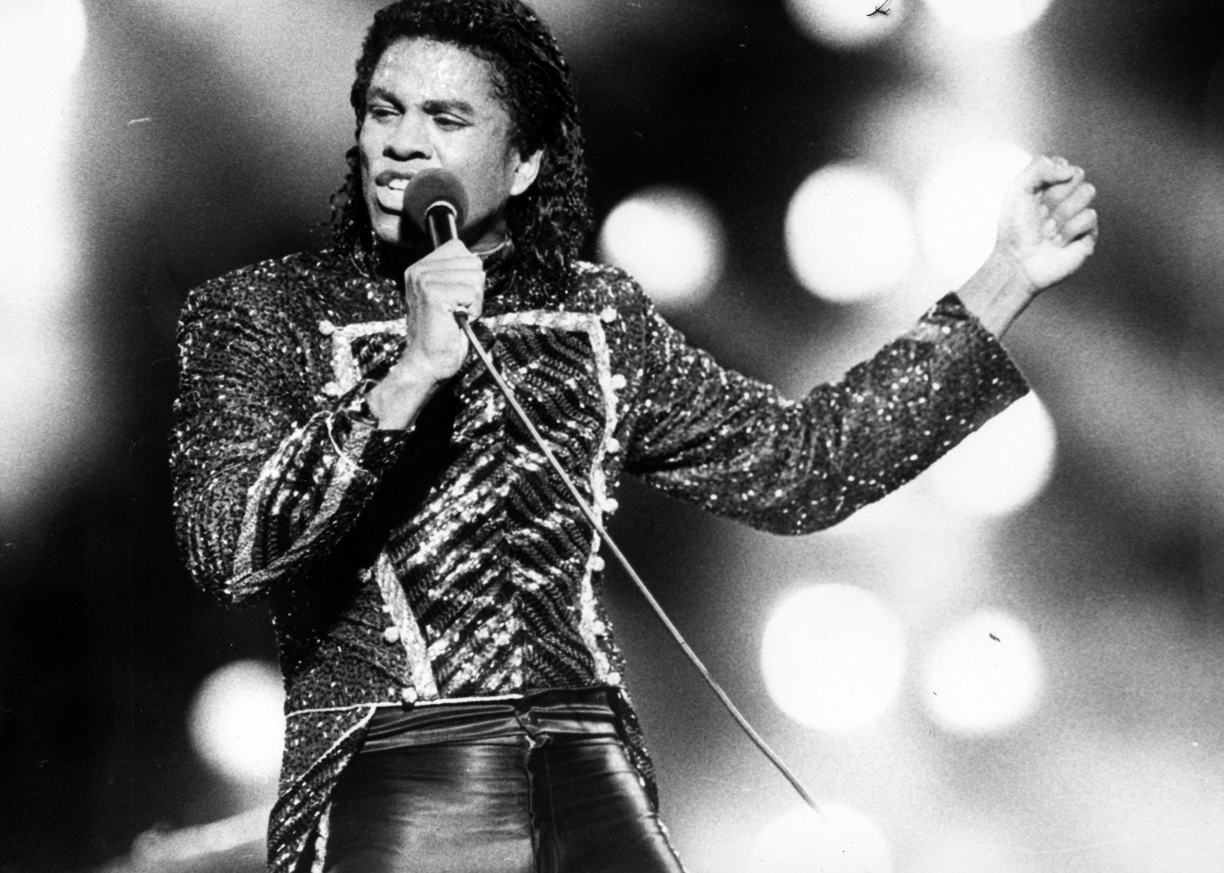 Jermaine Jackson performs live on stage at a concert and holds a microphone.