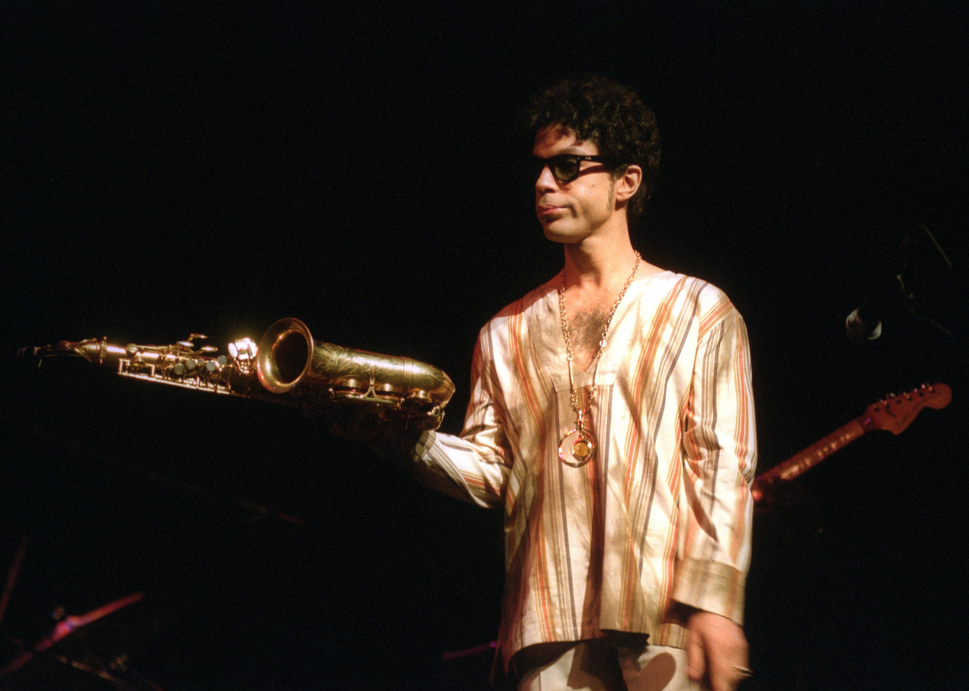 Prince holding Maceo Parker's alto saxophone in concert at Apollo Theater.