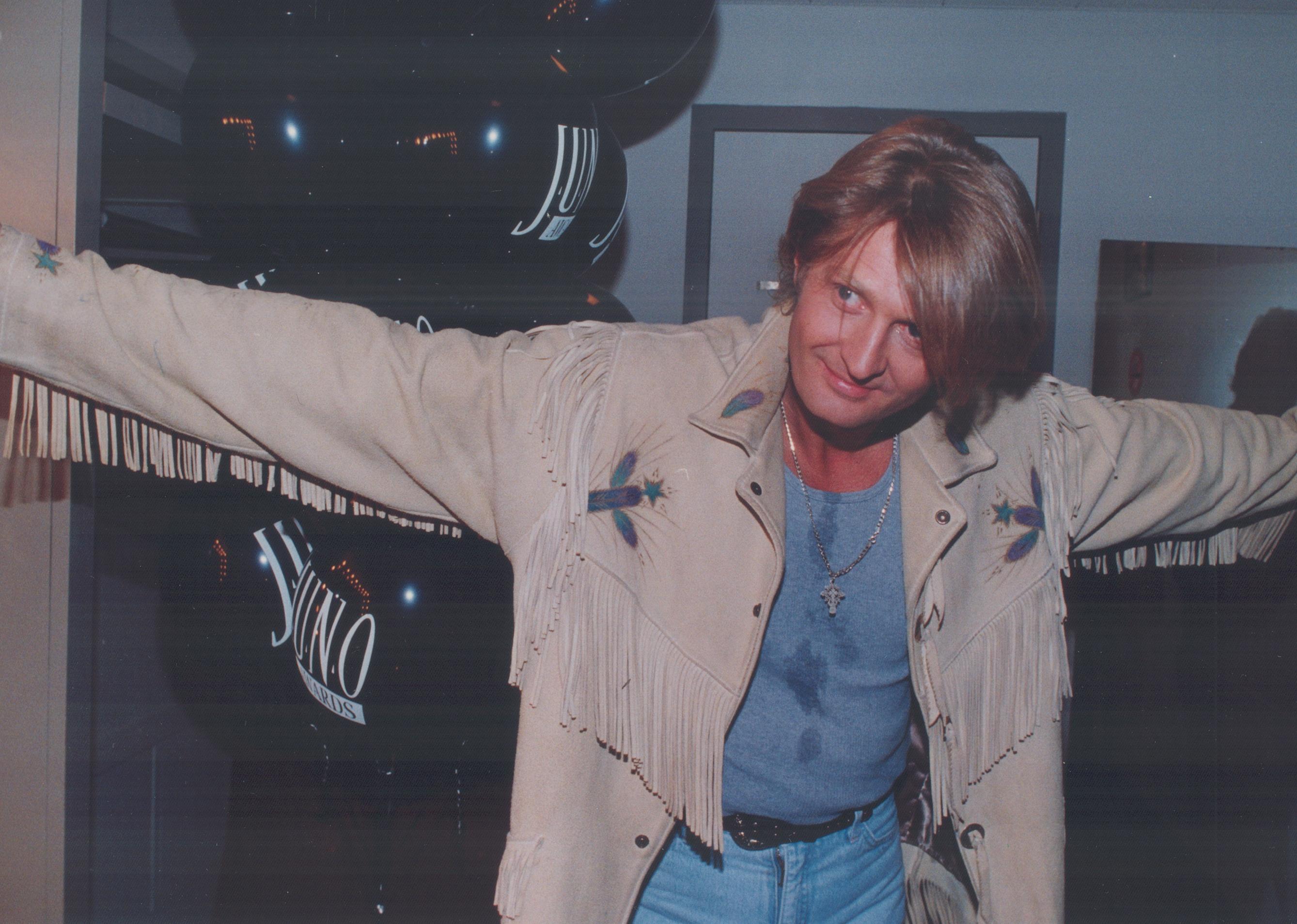 Tom Cochrane standing with arms spread.