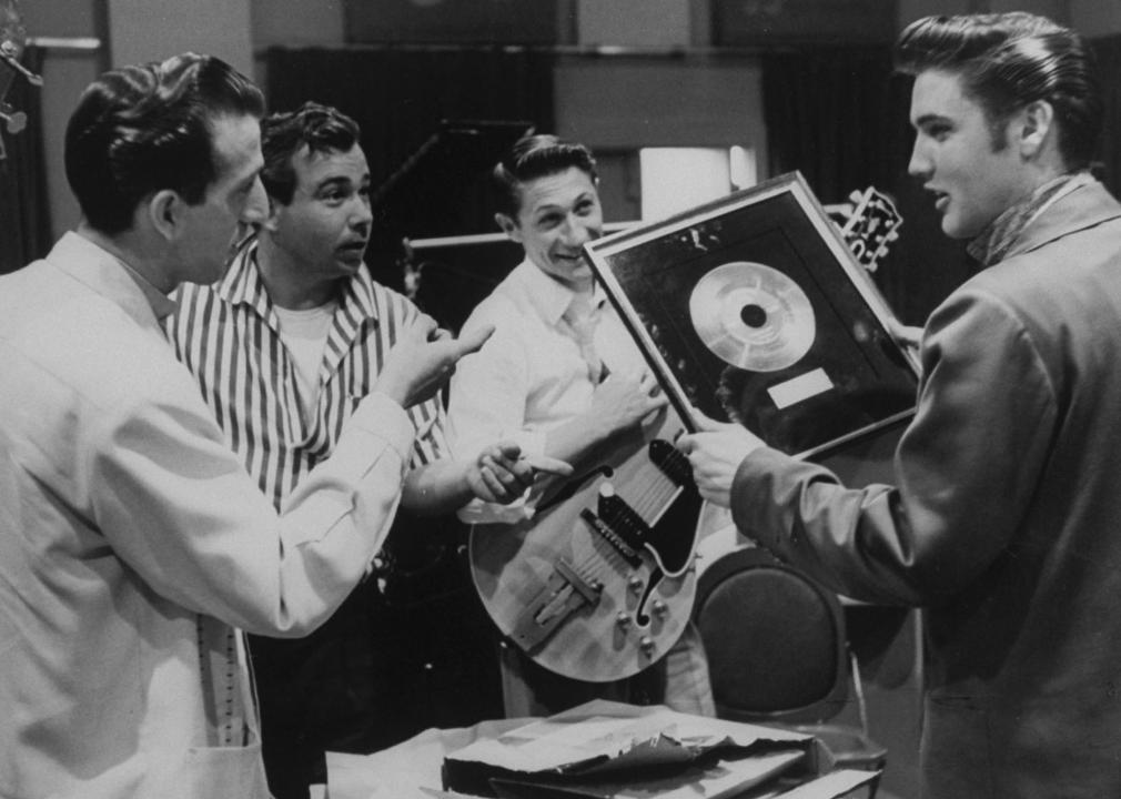 Elvis Presley showing framed gold record of Heartbreak Hotel.