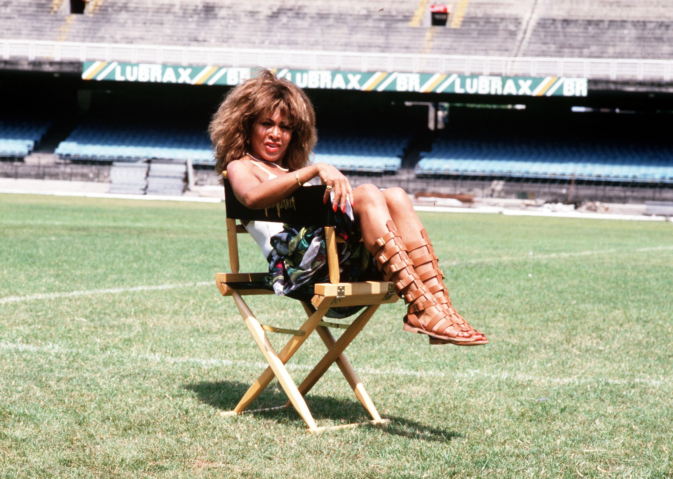 Tina Turner sitting in a chair on the field of a stadium in Rio de Janeiro, Brazil.