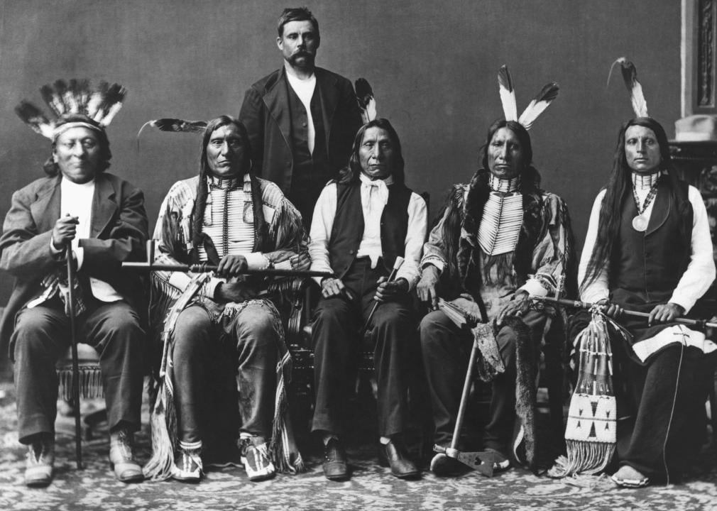 A group photo of several Indigenous men, with some wearing traditional clothing and headdresses.