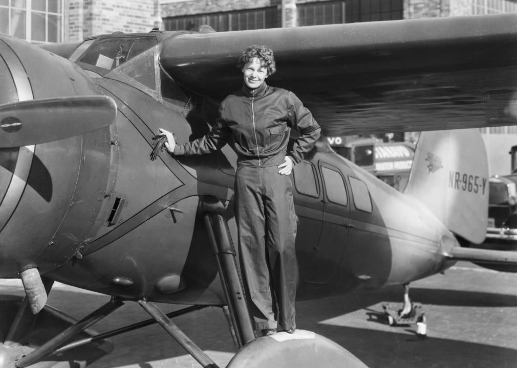 Amelia Earhart poses beside plane.