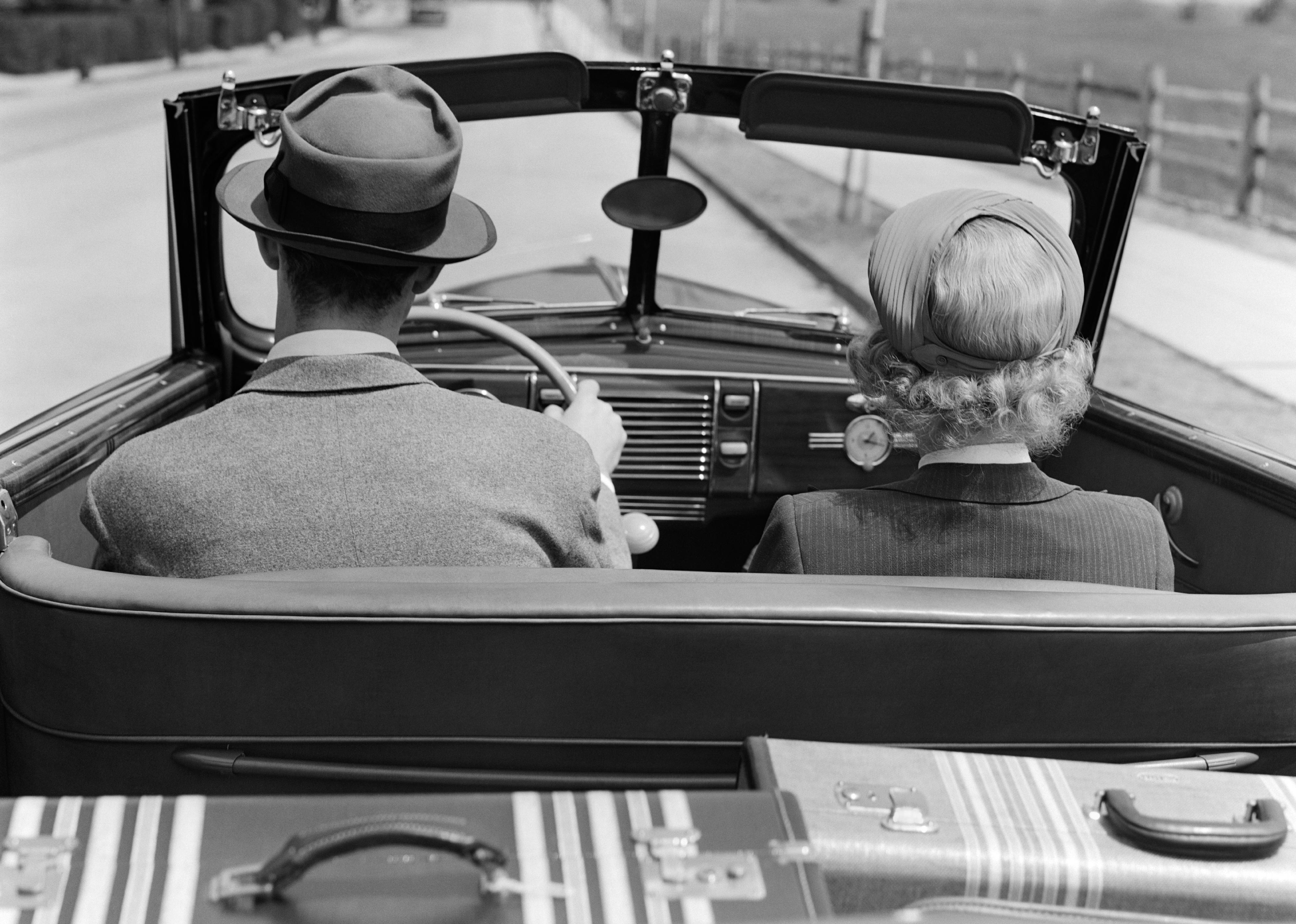 Rear view of 1930s couple driving down road.