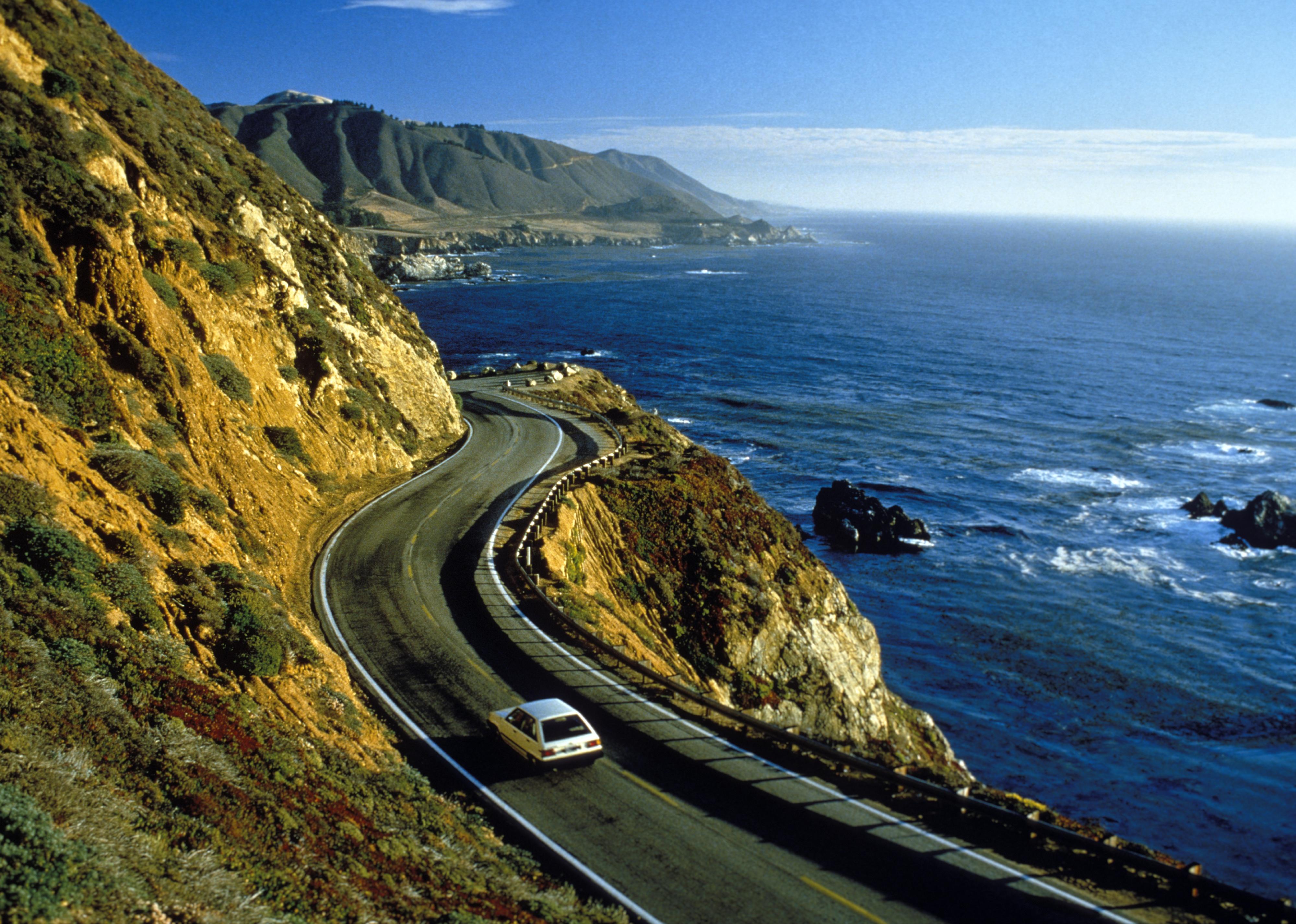 Car driving on highway between cliffs and ocean. 