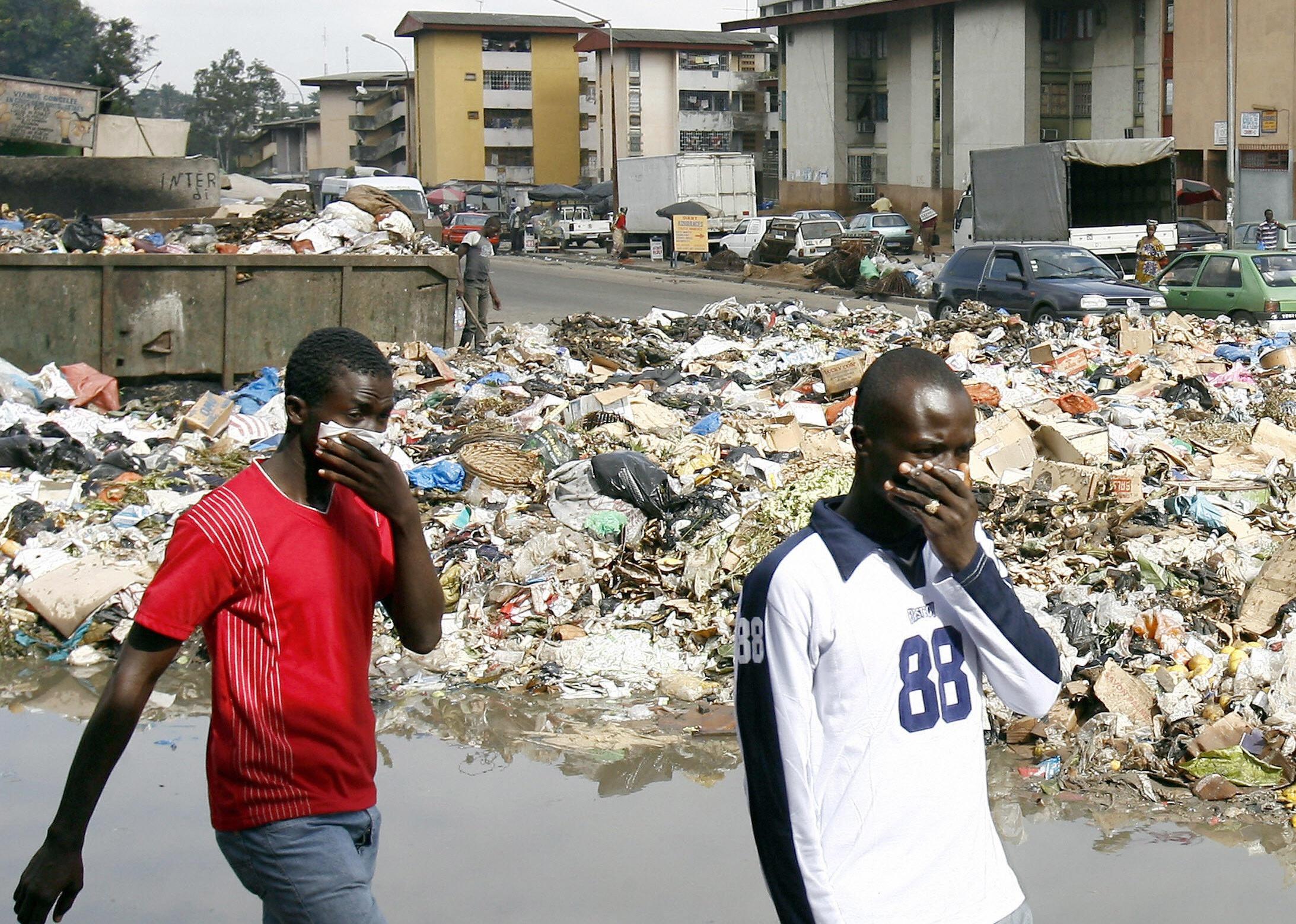  Men protect themselves from the smell in front of a dump in an Abidjan district.