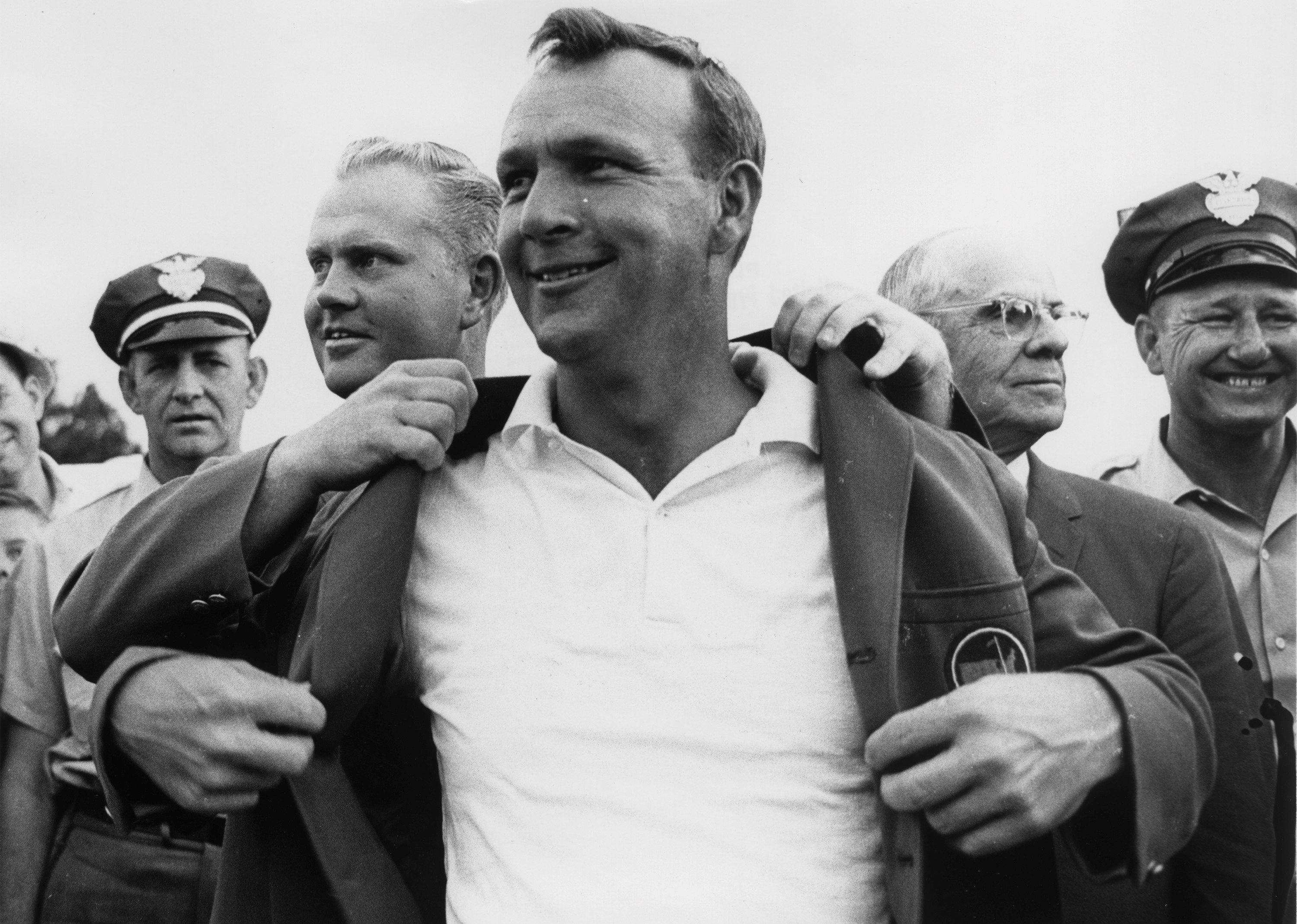 Arnold Palmer puts on the Masters Green Jacket with the help of Jack Nicklaus and Chairman Clifford Roberts.