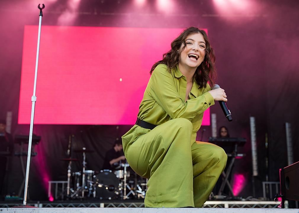 Lorde performing onstage in olive green outfit.