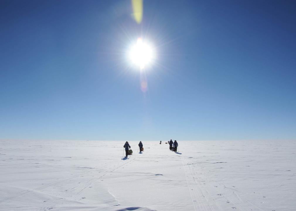People crossing a tabular iceberg on a sunny day.