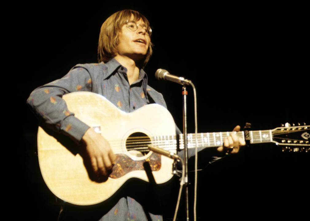 John Denver performing on stage with guitar.