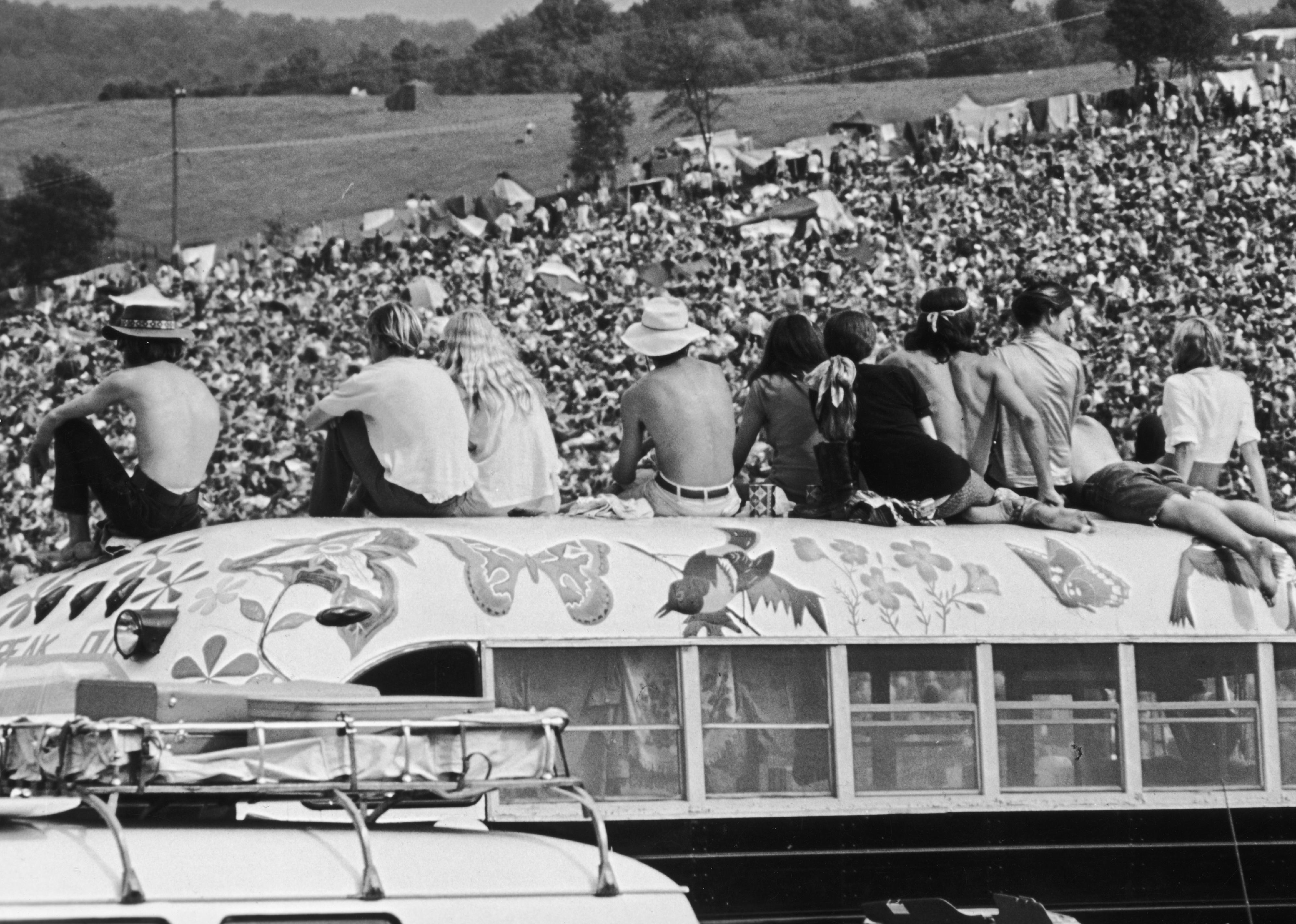 Fans sitting on top of a painted bus at the Woodstock Music Festival.
