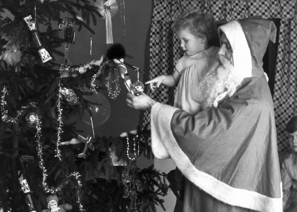 Man in Santa Claus costume holds child admires Christmas ornament.