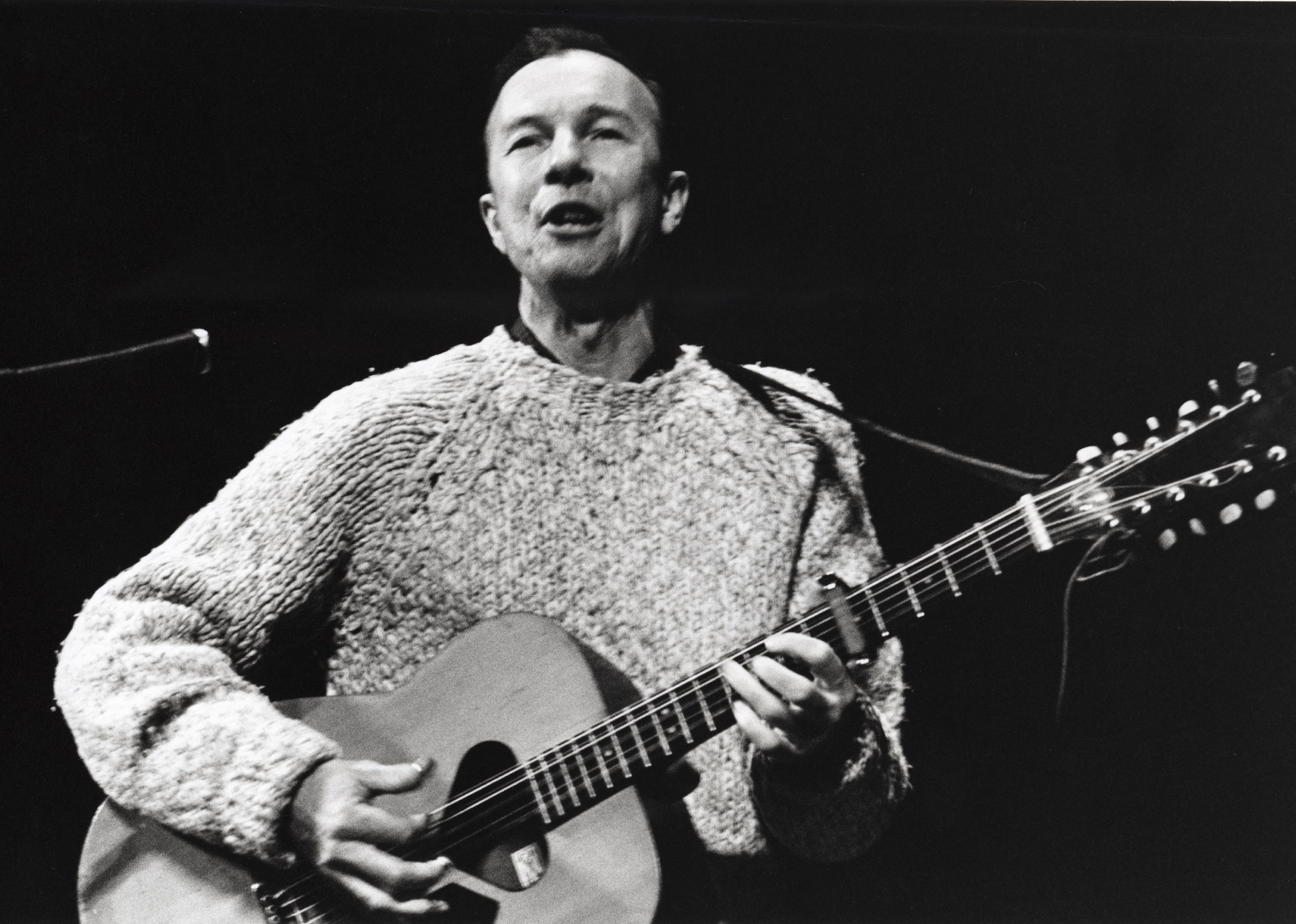 Pete Seeger performing on stage at a Paul Robeson benefit concert.