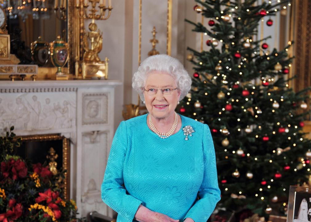 Queen Elizabeth poses with a Christmas tree behind her.