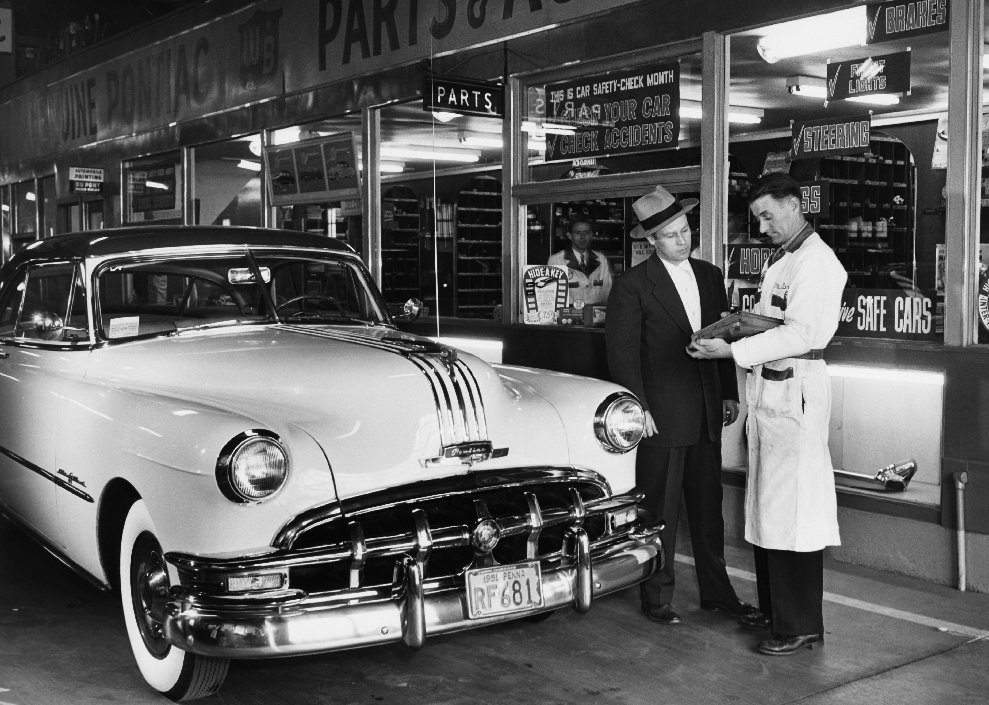 Mechanic showing bill to customer in front of a Pontiac.
