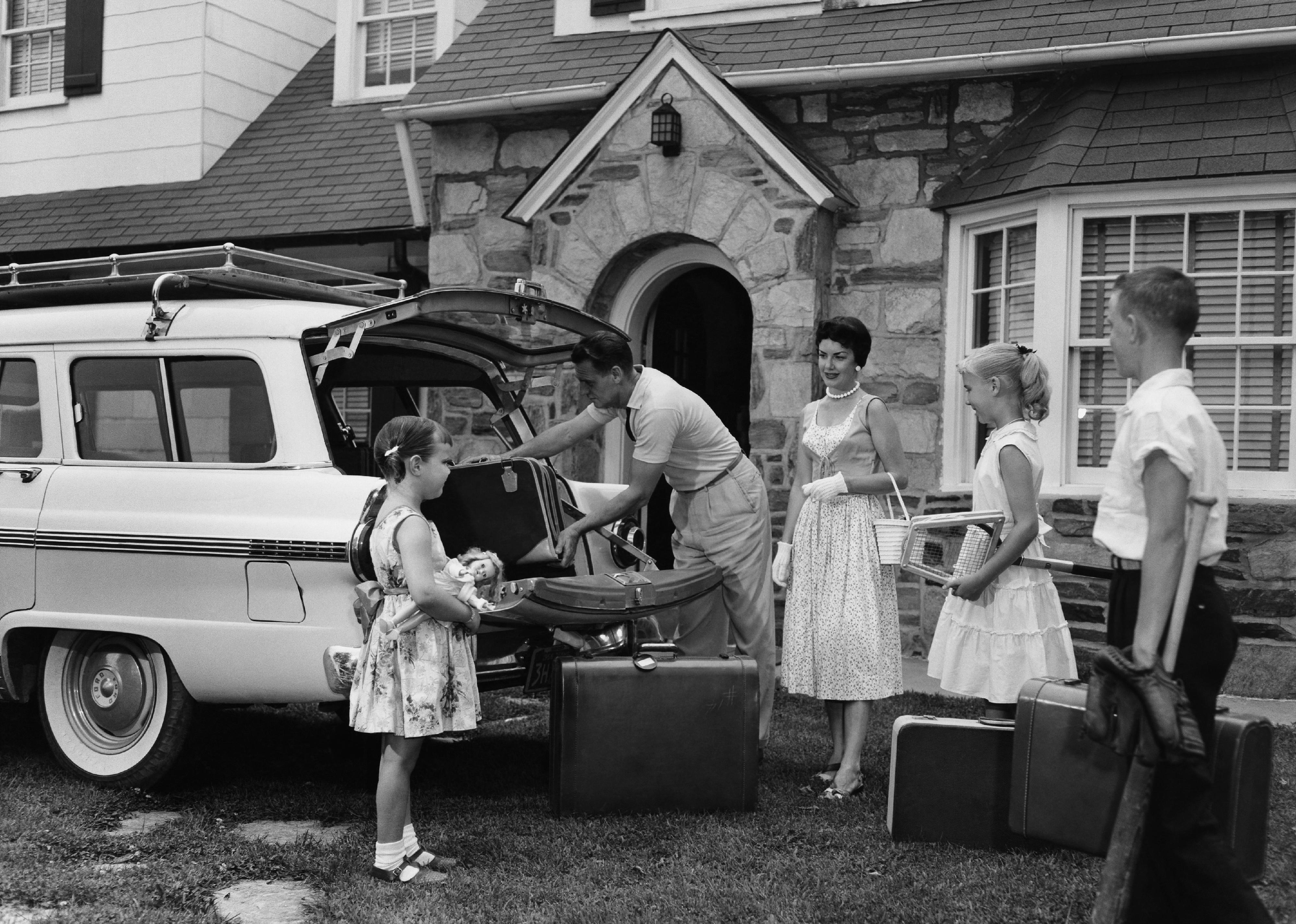 Family dressed in nice clothes, packing the car for trip.