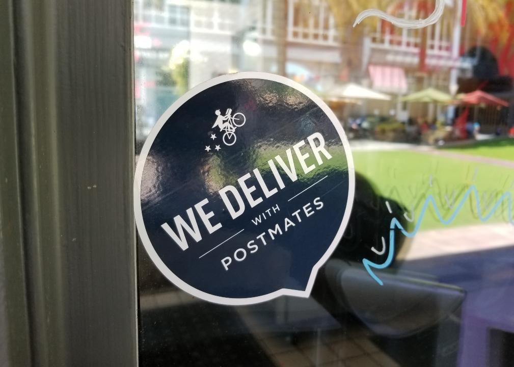 A close-up of logo on a door reading We Deliver With Postmates.