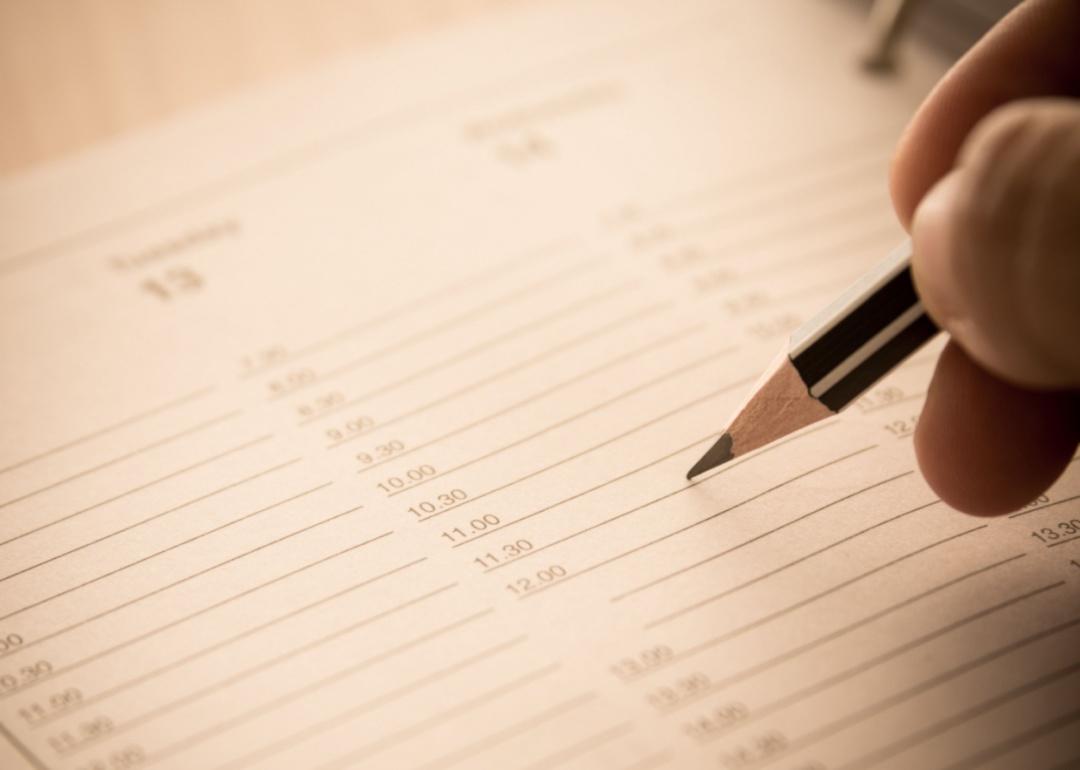 A hand holding a pencil on a calendar with times.