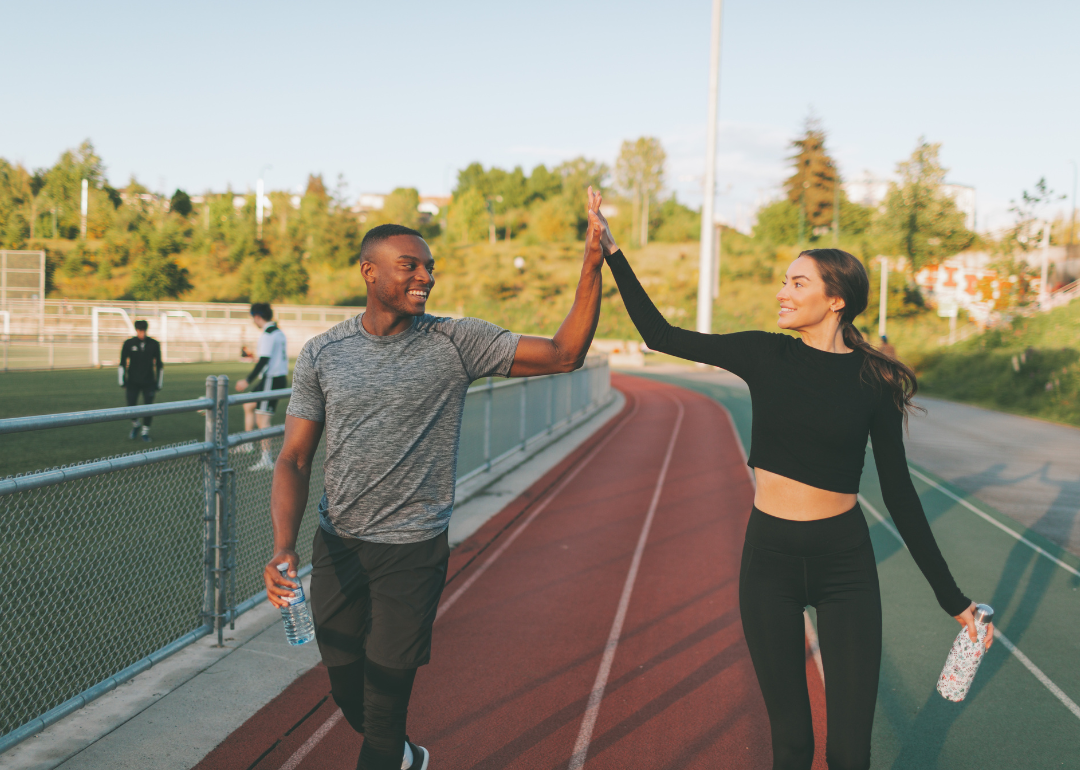 Two people high-fiving each other outside a track in exercise clothing.