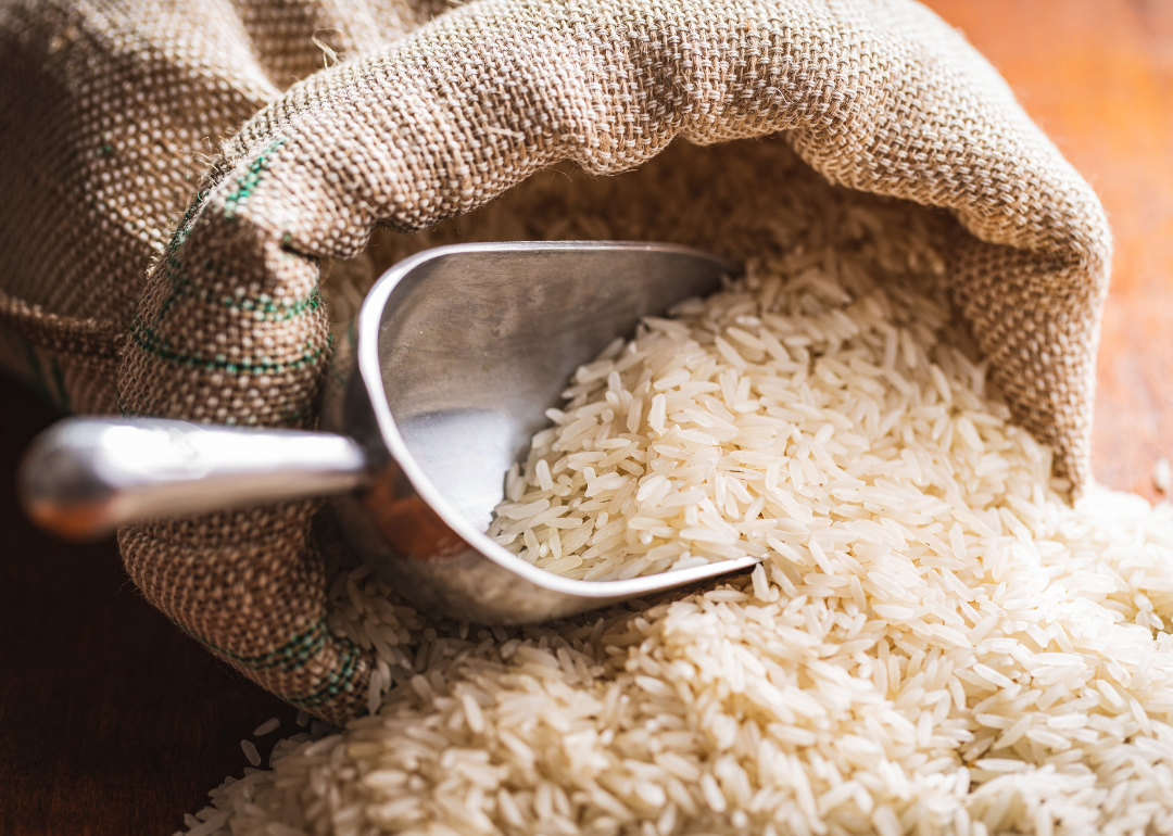 Uncooked white rice spilling out of a burlap sack on a wooden table