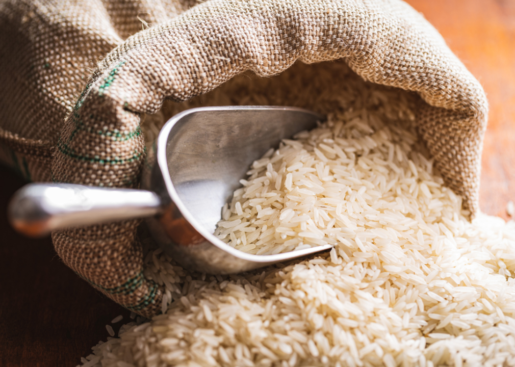 Uncooked white rice spilling out of a burlap sack on a wooden table.