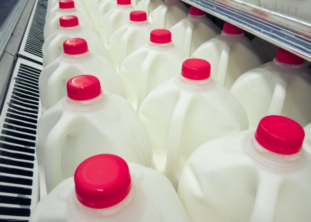 A grocery shelf filled with gallons of whole milk.