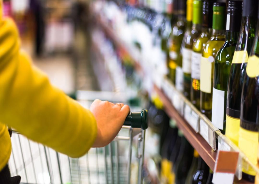 A person pushing a grocery cart down the wine aisle.