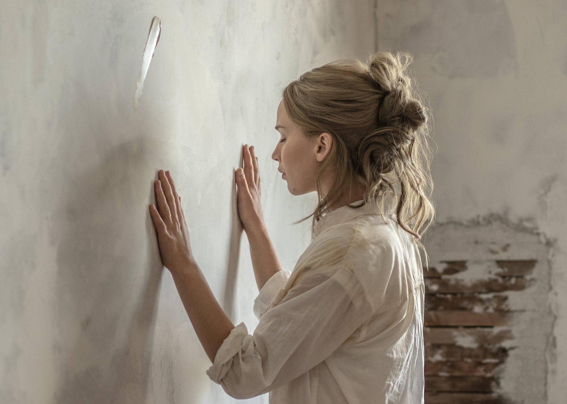 Jennifer Lawrence in an unfinished room with her hands on the wall.