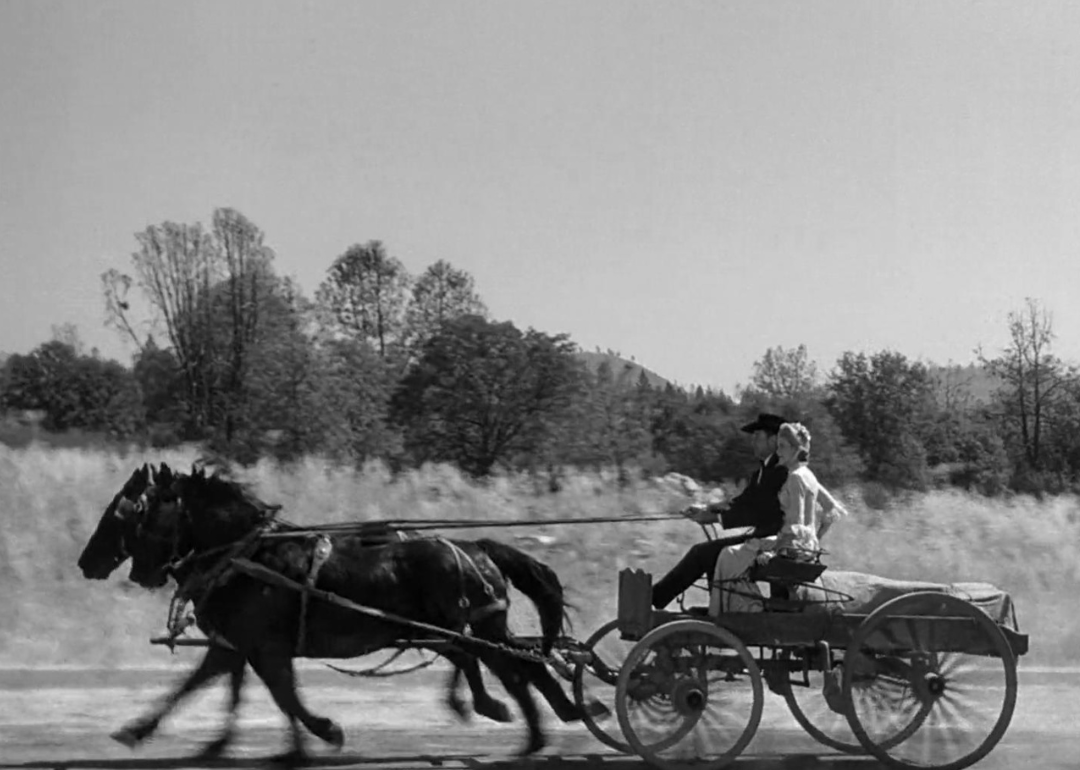 Gary Cooper and Grace Kelly speed down a road on horse and buggy.