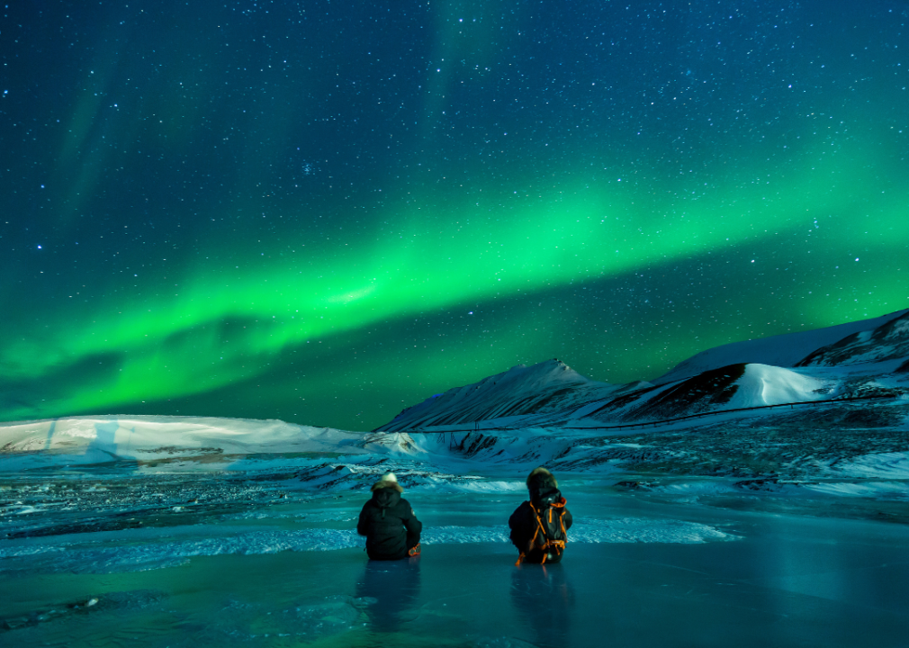 Two people under the green northern lights in Alaska.