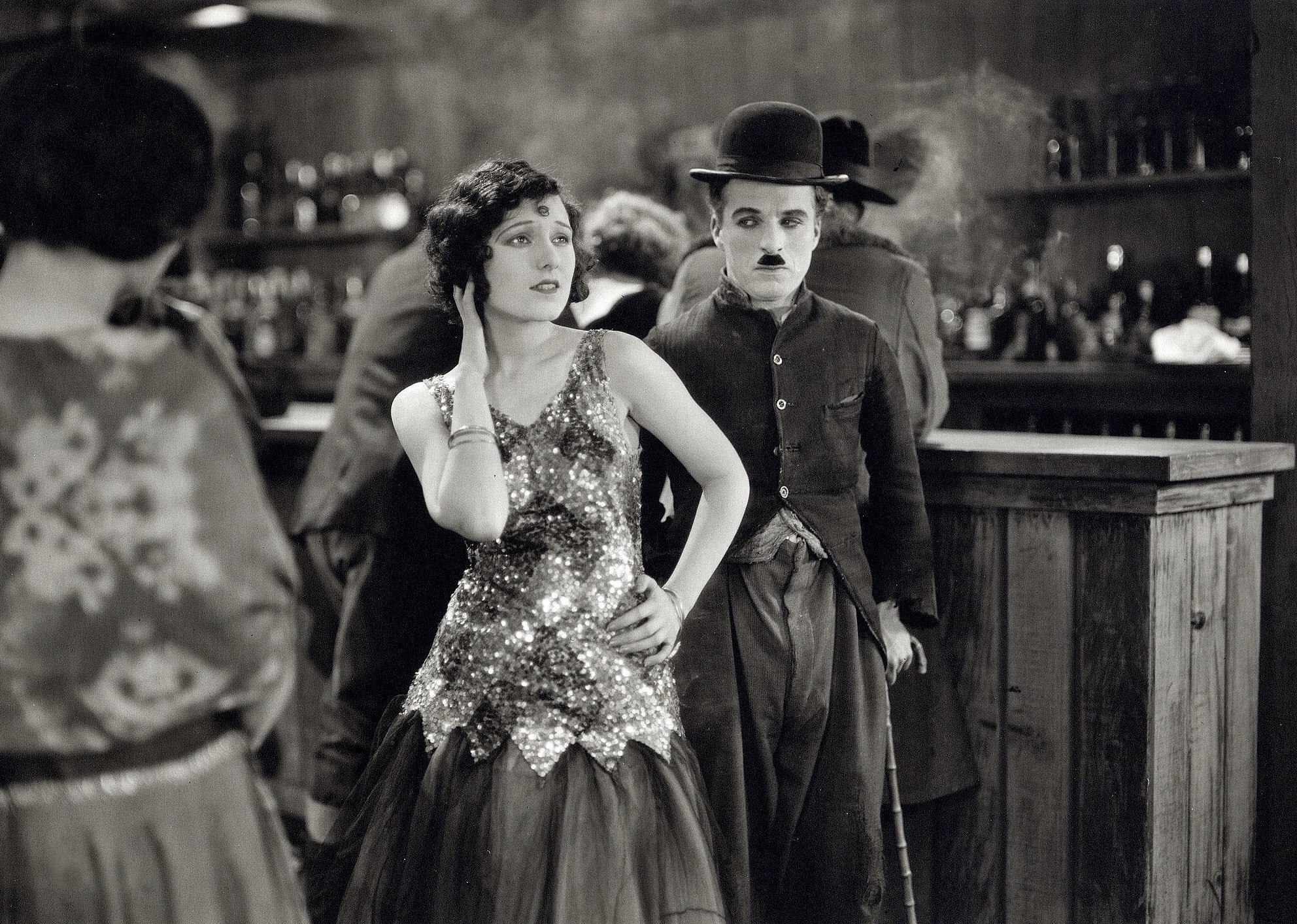 Charles Chaplin in a bar with a woman in a sparkly dress.
