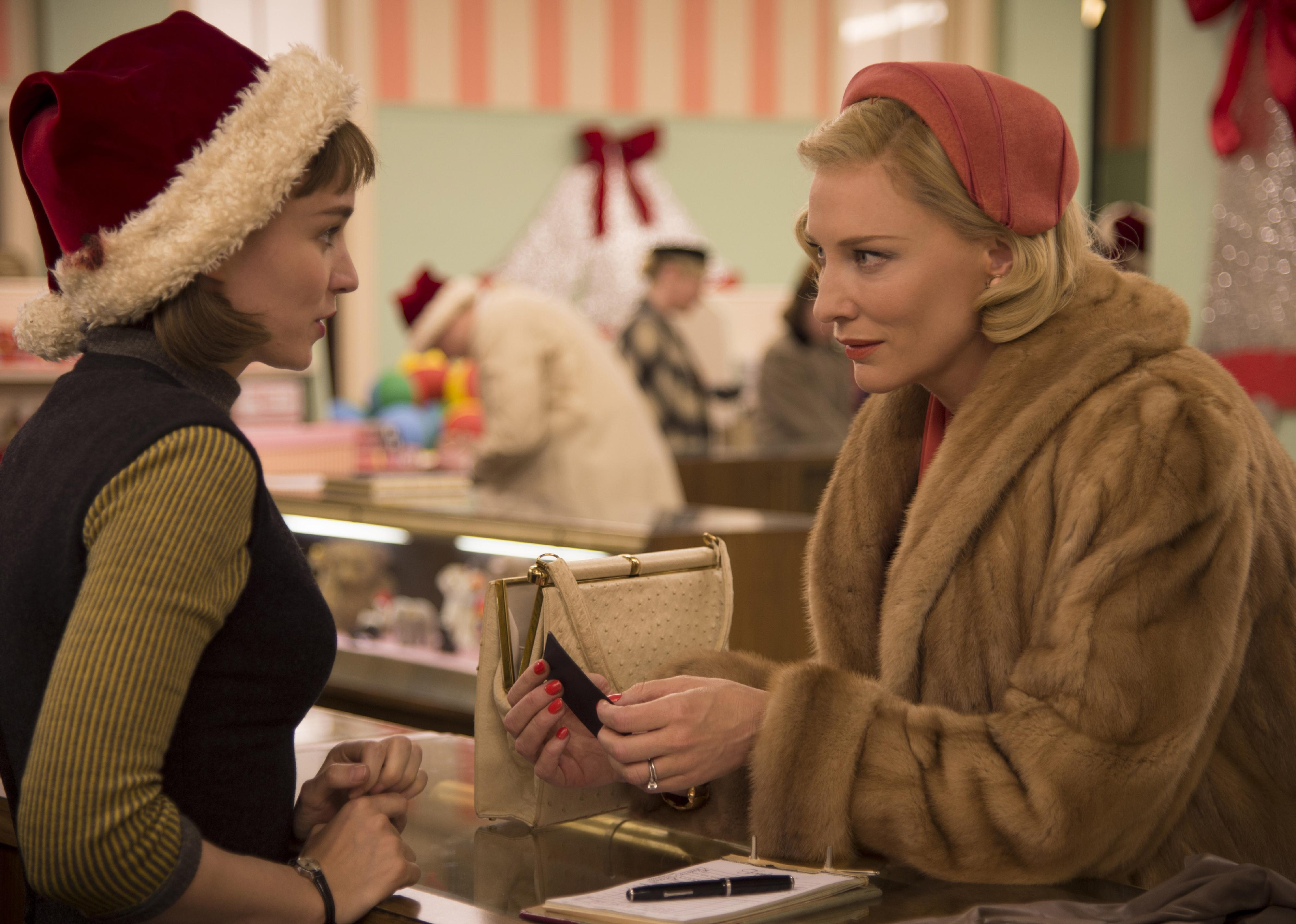 Rooney Mara in a Santa hat behind a counter talking to Cate Blanchett.