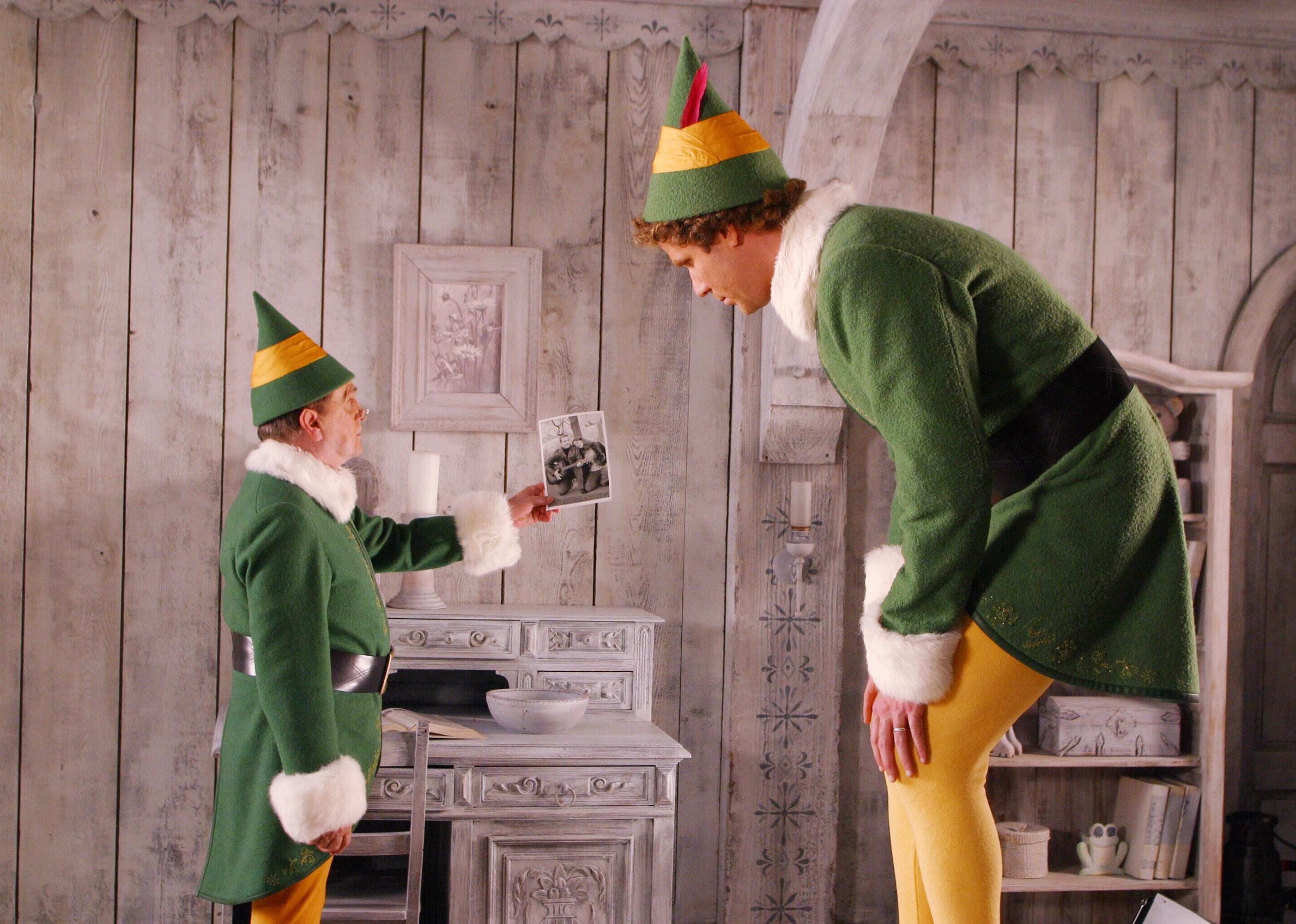 Bob Newhart as a small elf holds up a picture to Will Ferrell, who is considerably larger.