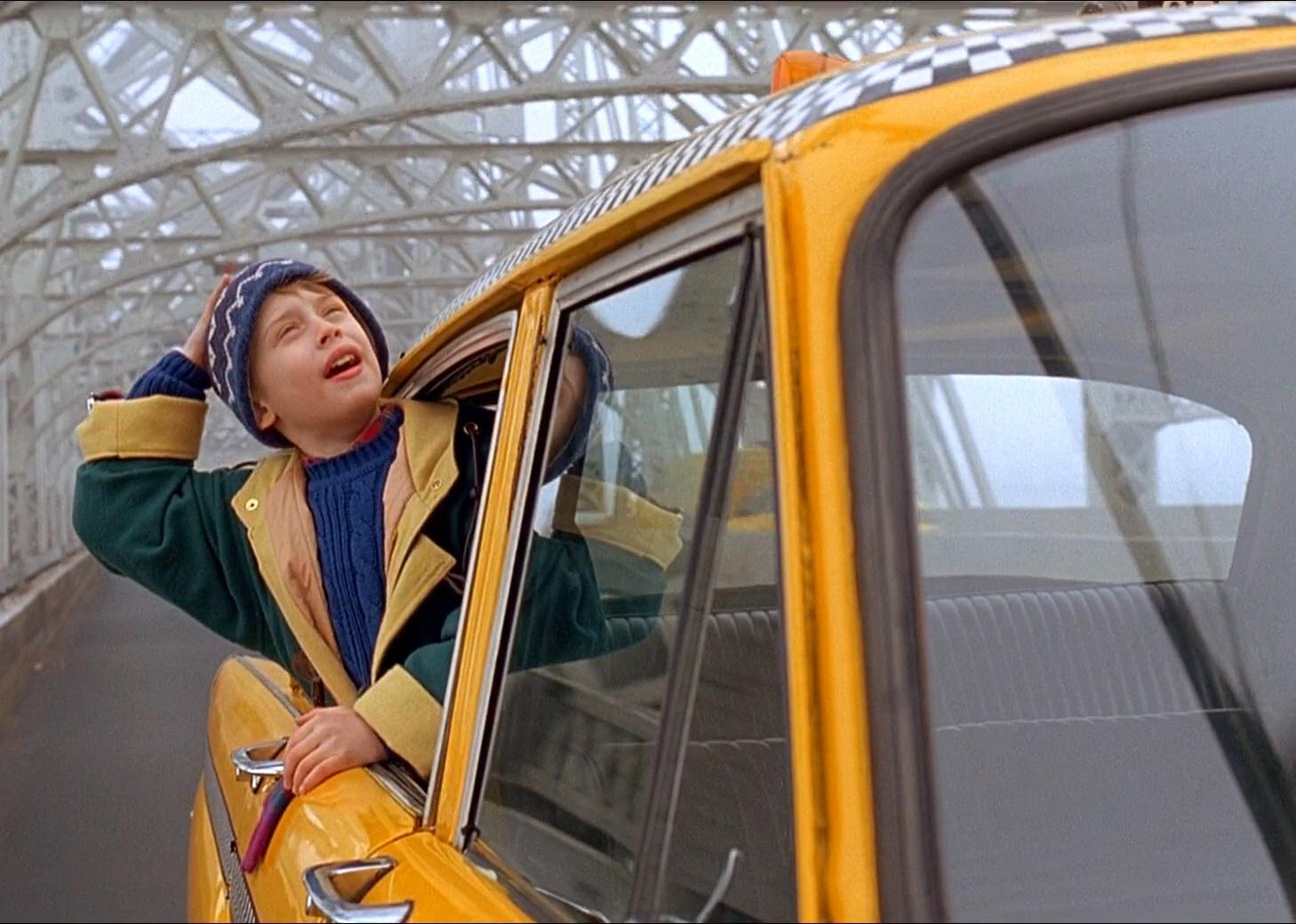 Macaulay Culkin hanging his head out of a yellow cab while it speeds over a bridge.