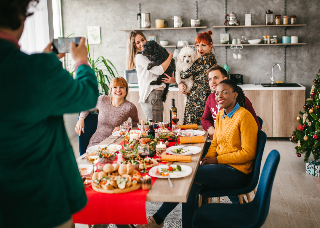 Two people hold dogs behind a dinner table of people posing for a holiday picture.