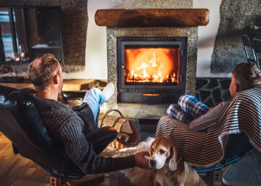 A father and son sit by the fire with a small dog.