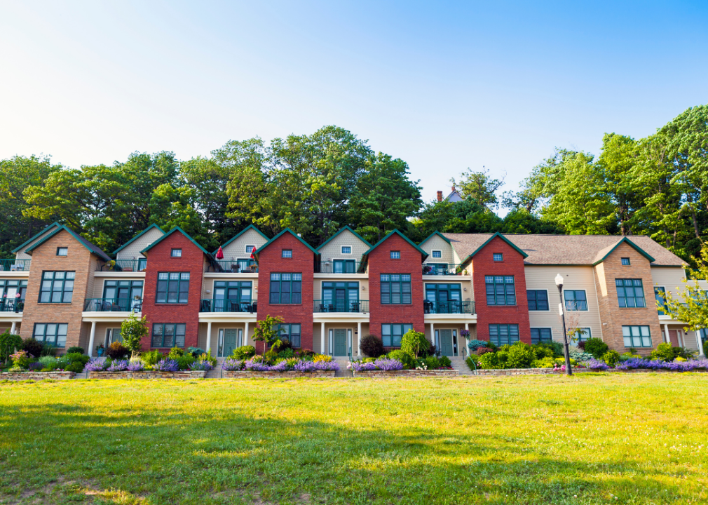 Row of multi-level townhomes with pretty landscaping and a green field in front.