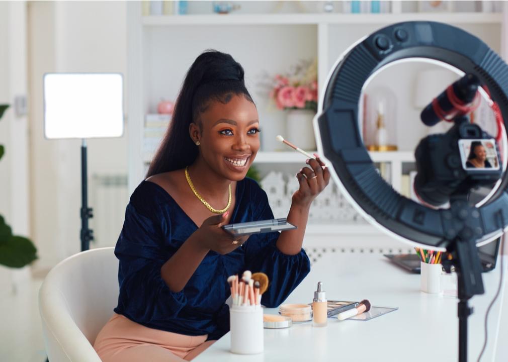 Young woman demonstrating with makeup and brushes while smiling on camera.