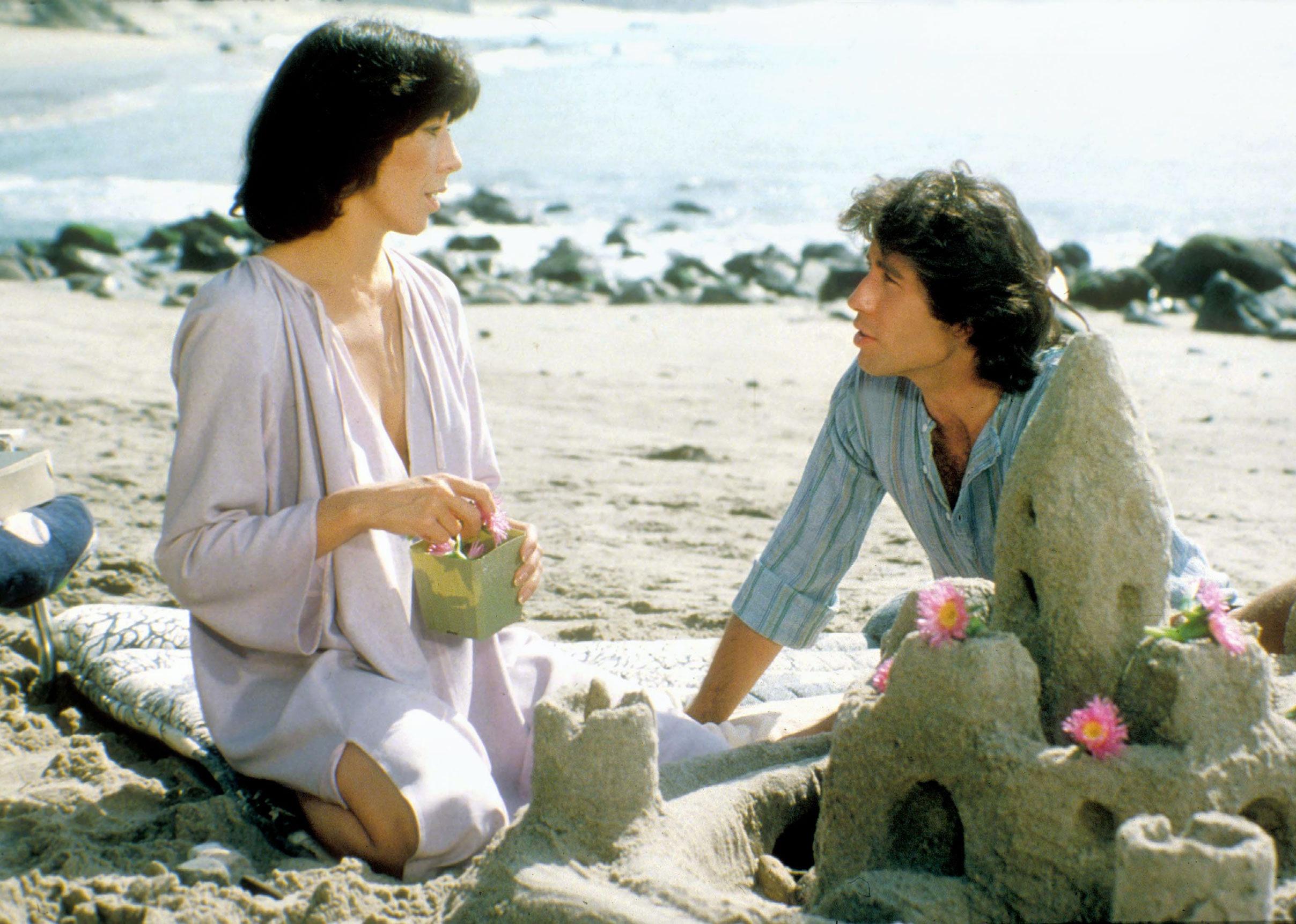 John Travolta and Lily Tomlin decorating a sandcastle on the beach.