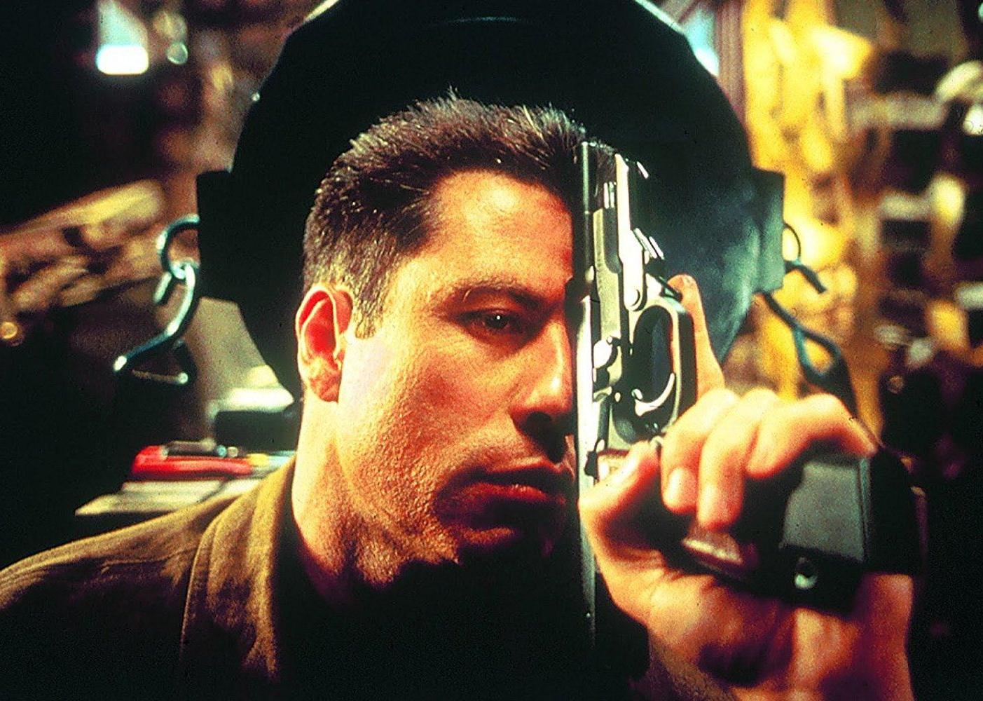 John Travolta holding a gun up against his face like he's thinking.