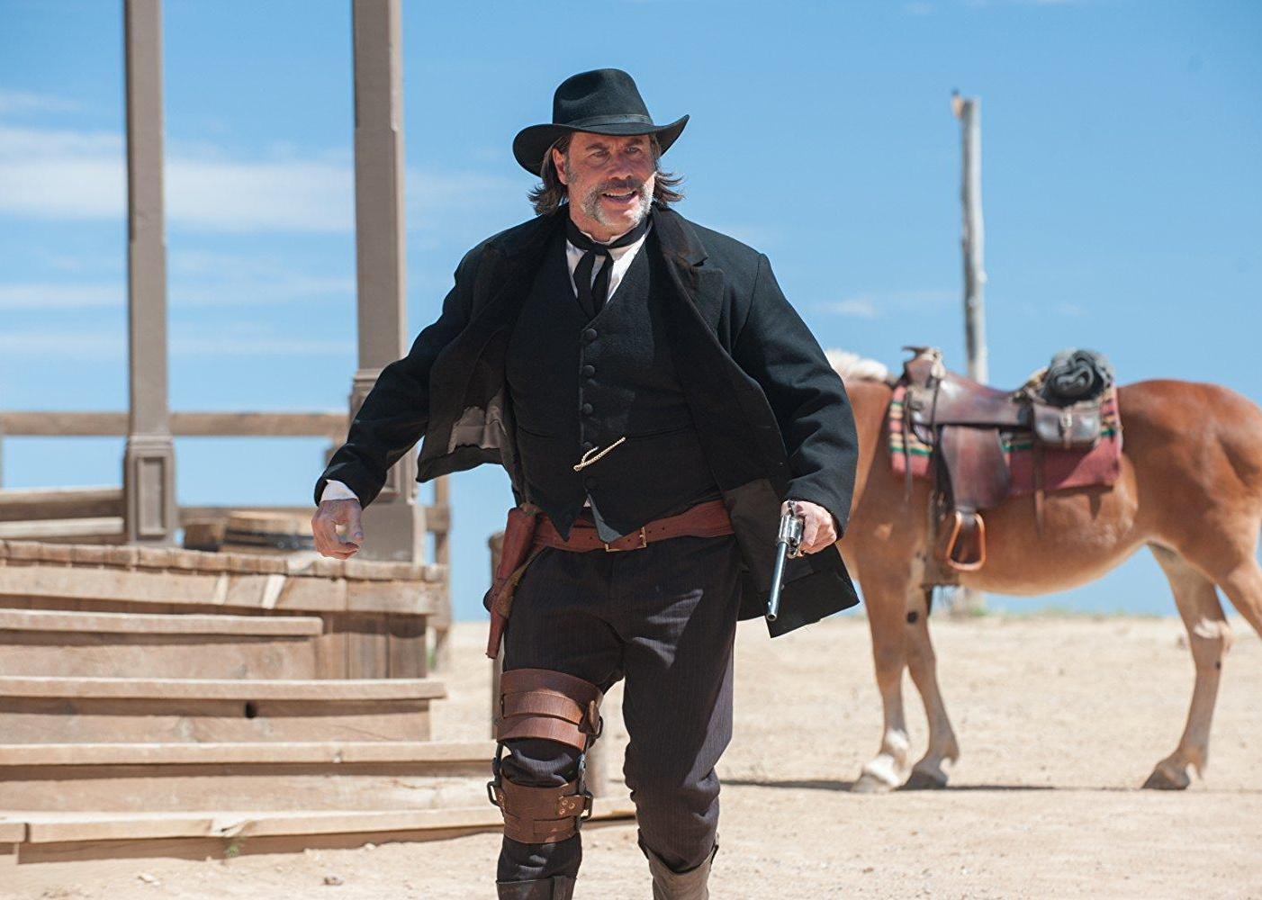 John Travolta in a black western suit and cowboy hat walking away from a horse.