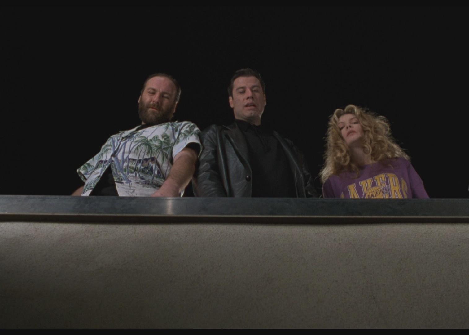 John Travolta, Rene Russo, and James Gandolfini looking down from the top of a building.