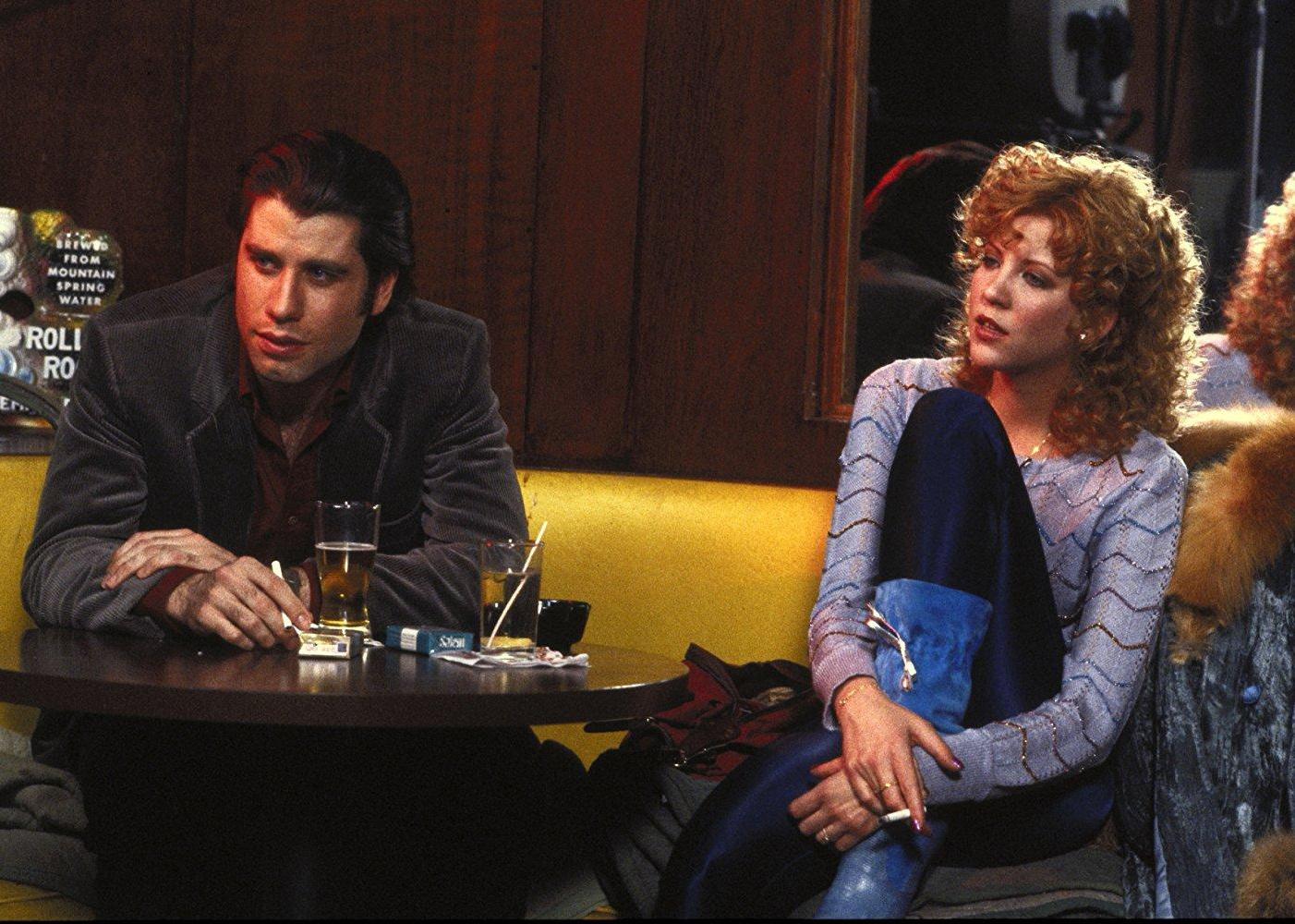 John Travolta drinking beers at a booth with a woman.