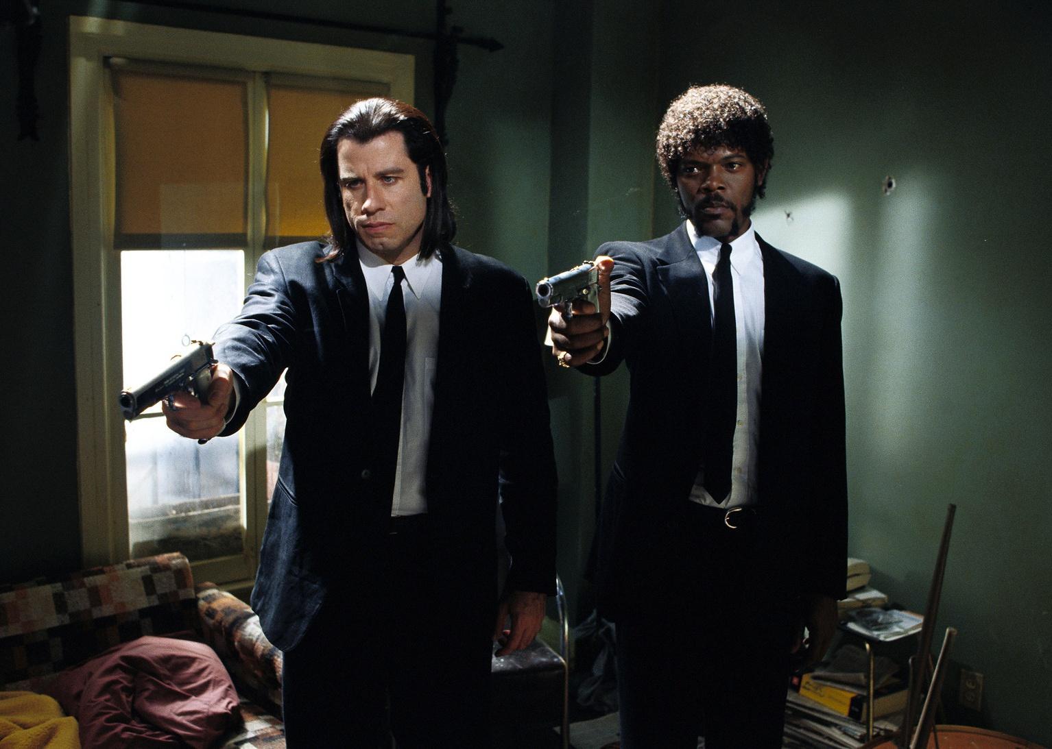 John Travolta and Samuel L. Jackson in black suits pointing guns.