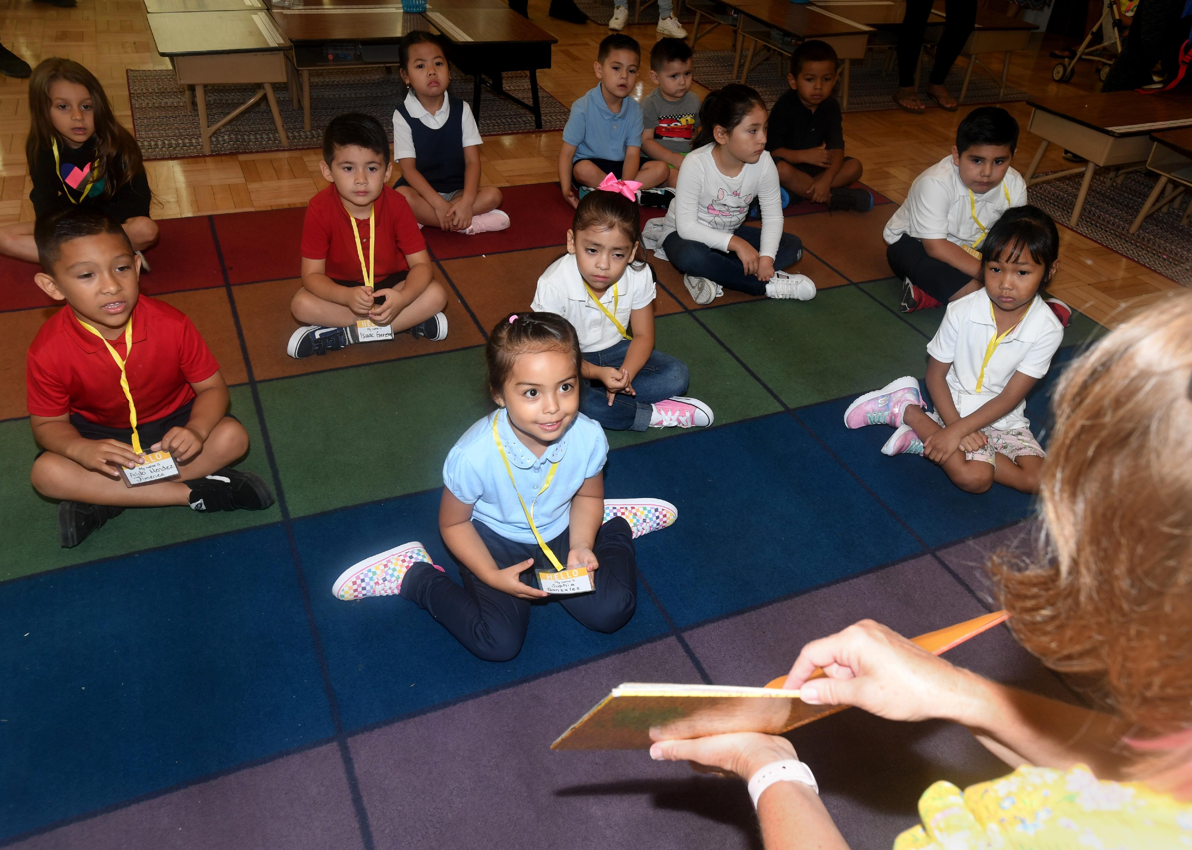 Students gathered around a teacher reading a book.